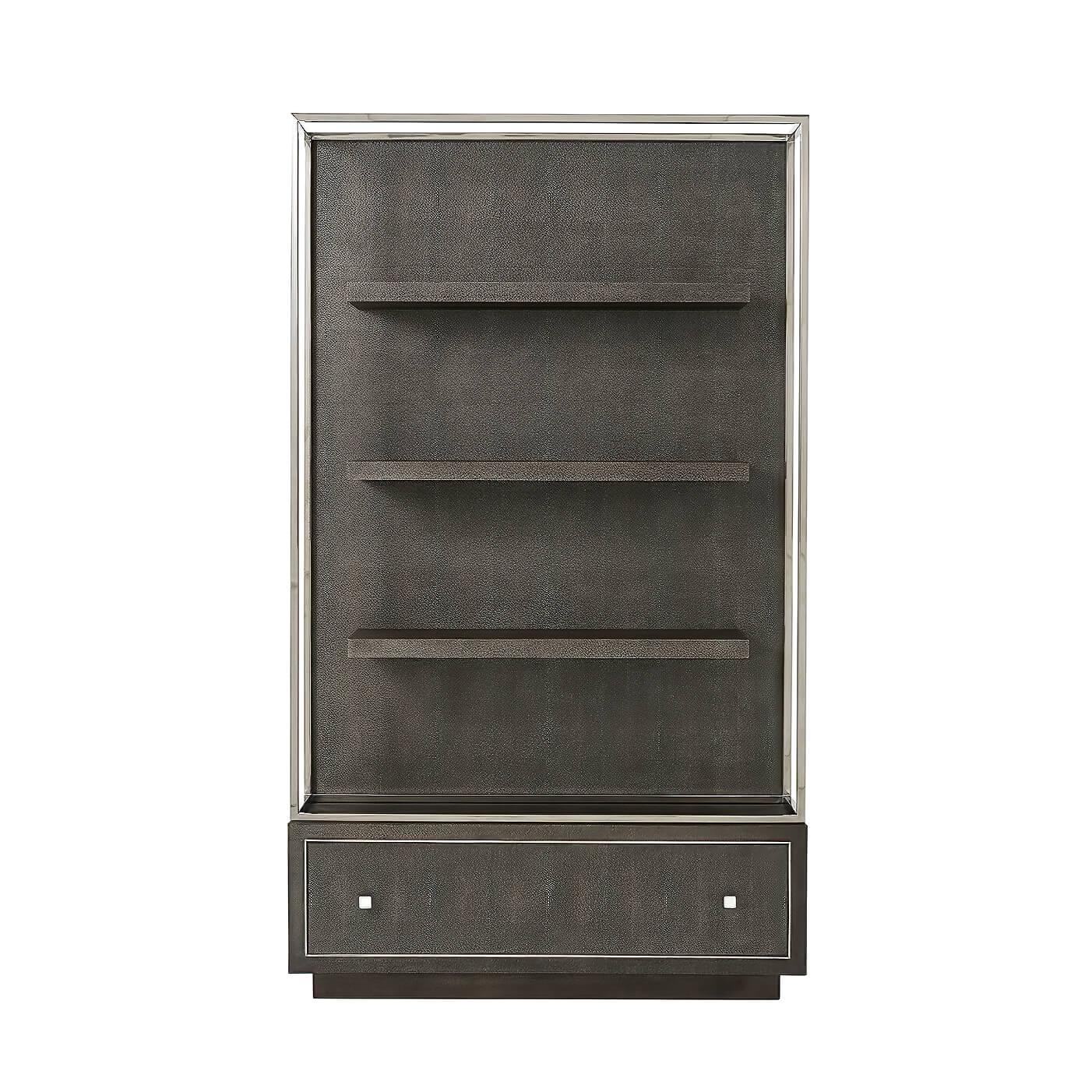 A modern bookcase with a polished nickel frame and covered in a dark grey Shagreen embossed leather wrap, with floating shelves and a large bottom drawer also with polished nickel hardware and moldings.
Dimensions: 48