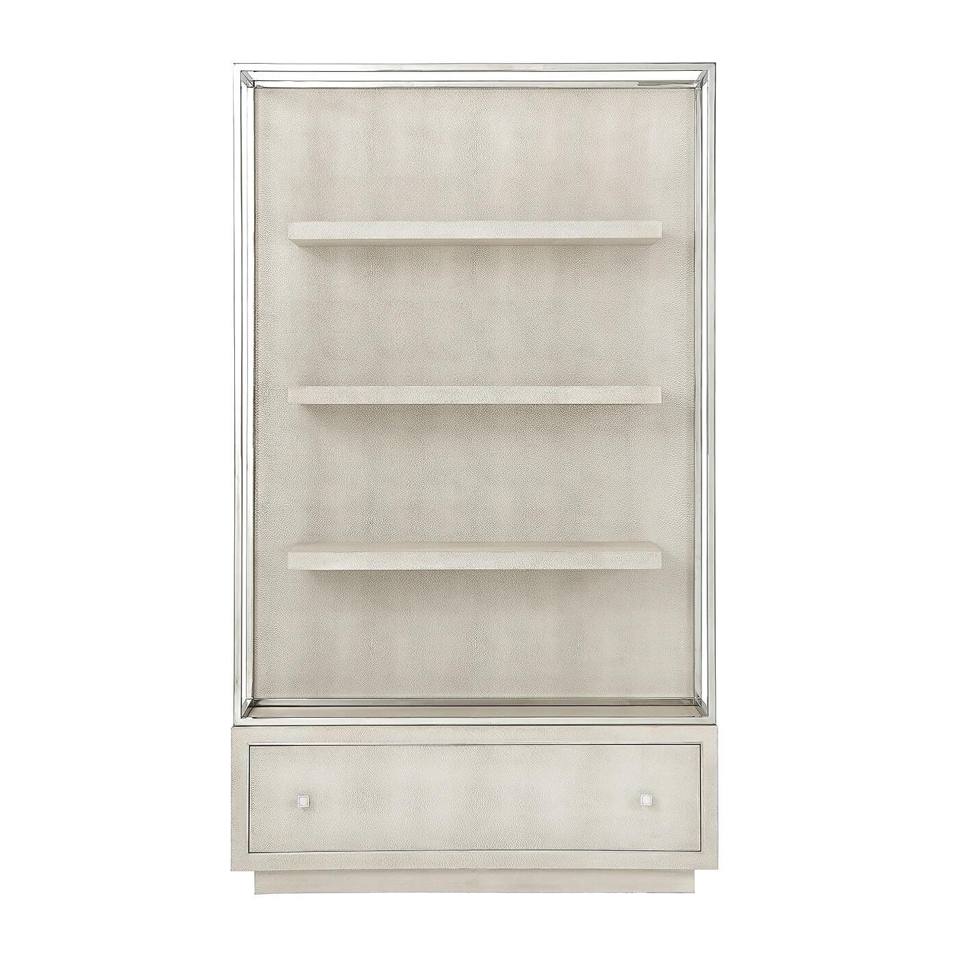 A modern bookcase with a polished nickel frame and covered in a light shagreen embossed leather wrap, with floating shelves and a large bottom drawer also with polished nickel hardware and moldings.
Dimensions: 48