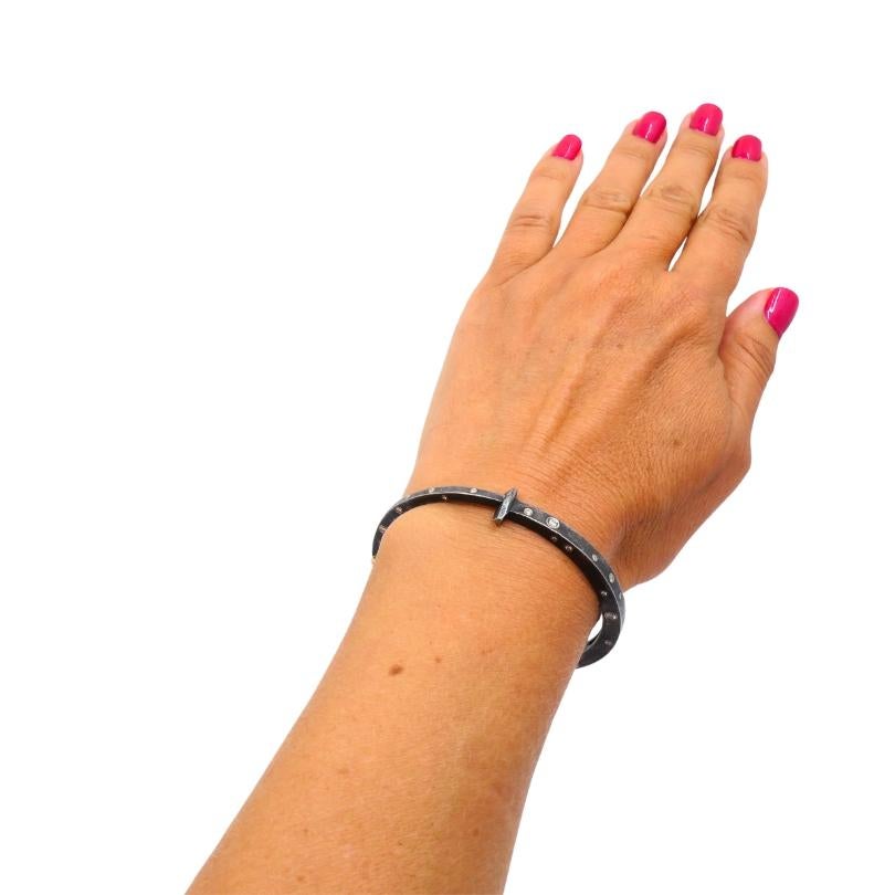 Una moderna pulsera brazalete de plata y oro amarillo de 18 quilates, con detalles de diamantes. u2028La pulsera está diseñada como una fina banda de plata con un acabado ligeramente oscurecido. Los pequeños detalles de diamantes redondos añaden un
