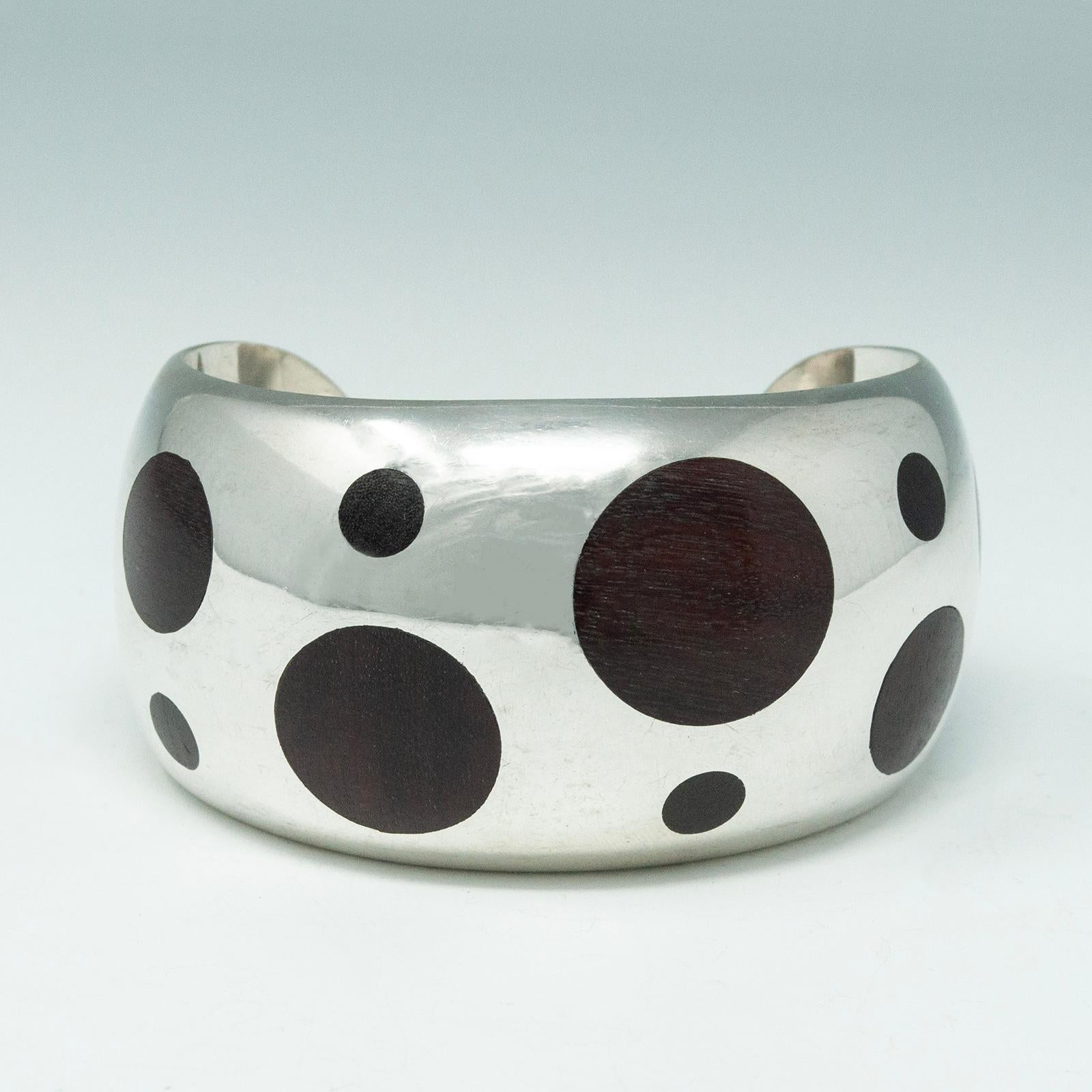 Modern silver and rosewood cuff

A beautiful silver cuff with inlaid rosewood circles, inspired by the 1960s William Spratling design. Marked Mexico 925, it measures 2.5 inches in diameter with a 1.25 inch gap. It's 1.63 inches wide, 80 grams.
