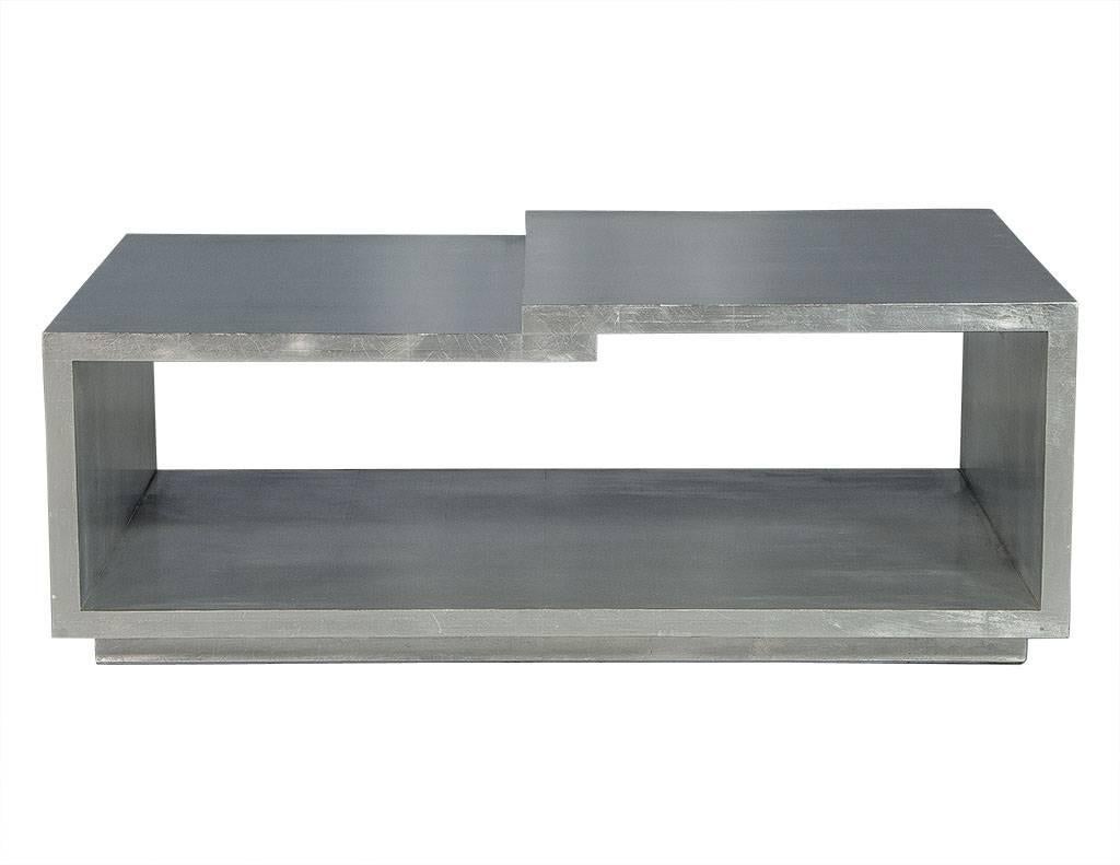 This modern cocktail table has a gorgeous, silver leaf brushed metal finish and open rectangular design. There are two levels to the top surface, one recessed, and the whole piece is full of character. A perfect addition to a luxe living