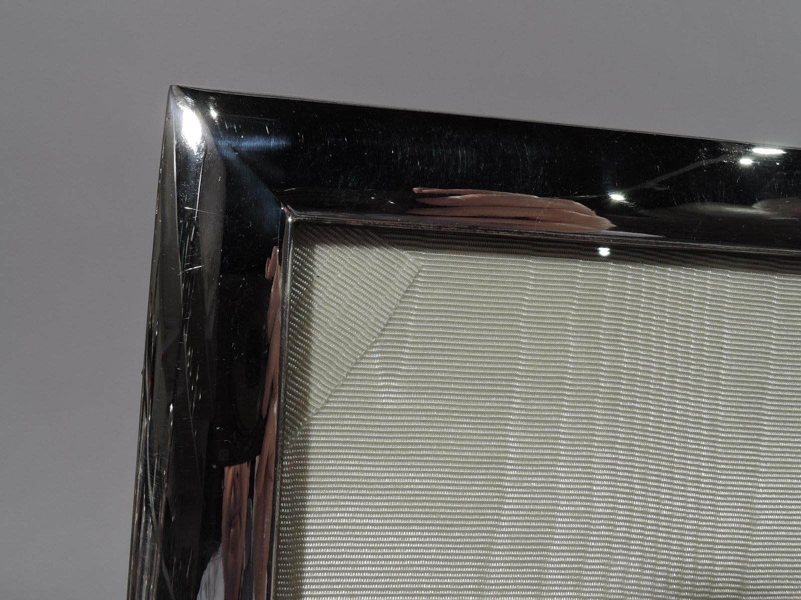 Modern sterling silver picture frame, circa 1950. Rectangular window in same surround with gently curved rails. With glass, silk lining, and wood back with unusual hinged support. Probably Japanese. Marked “Sterling 950”. 

Dimensions: Frame: H 11