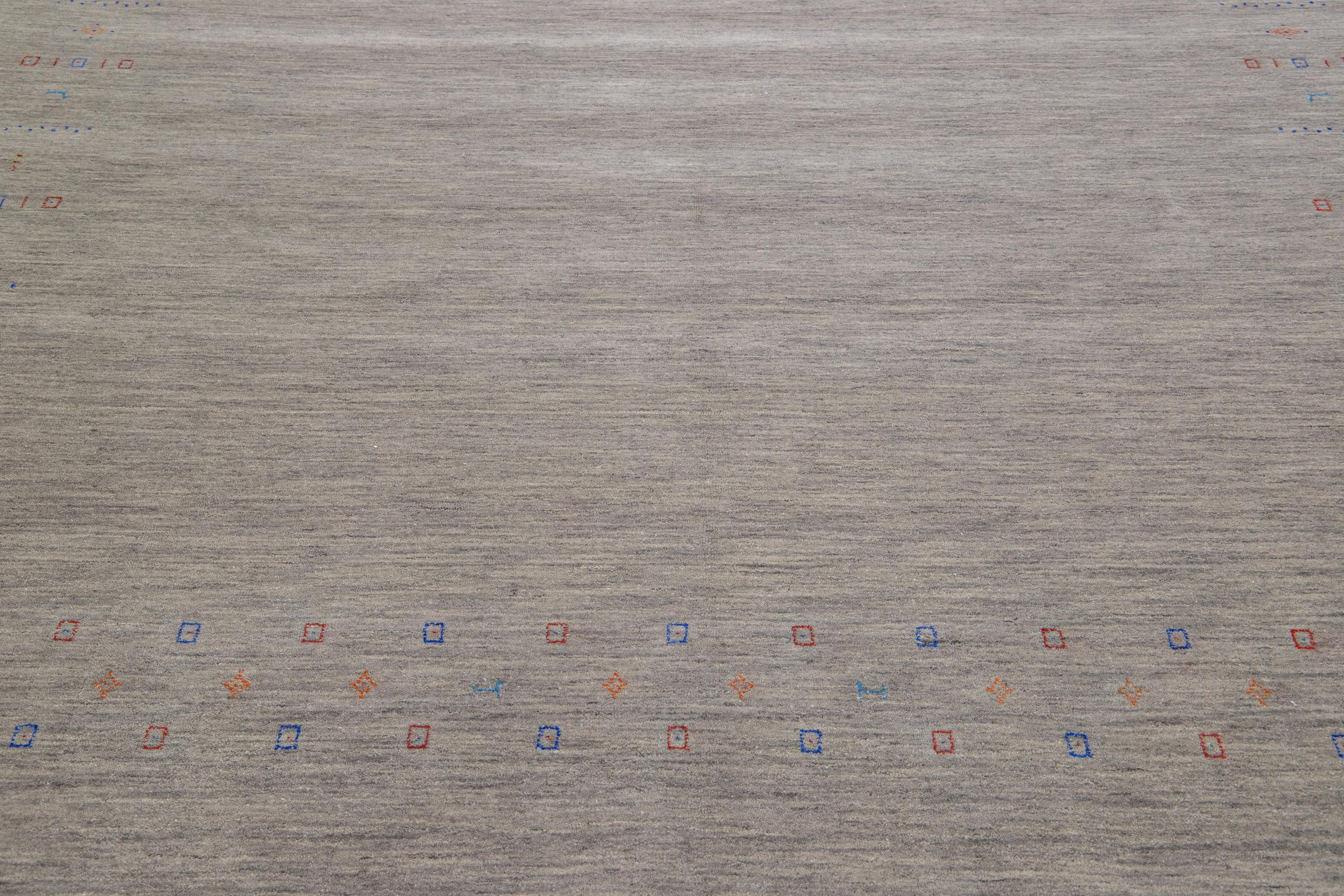 Dieser handgewebte Wollteppich im Gabbeh-Stil zeichnet sich durch ein graues und beiges Farbfeld aus, das eine minimalistische Ästhetik mit roten, blauen und orangen Akzenten aufweist.

Dieser Teppich misst: 8'7