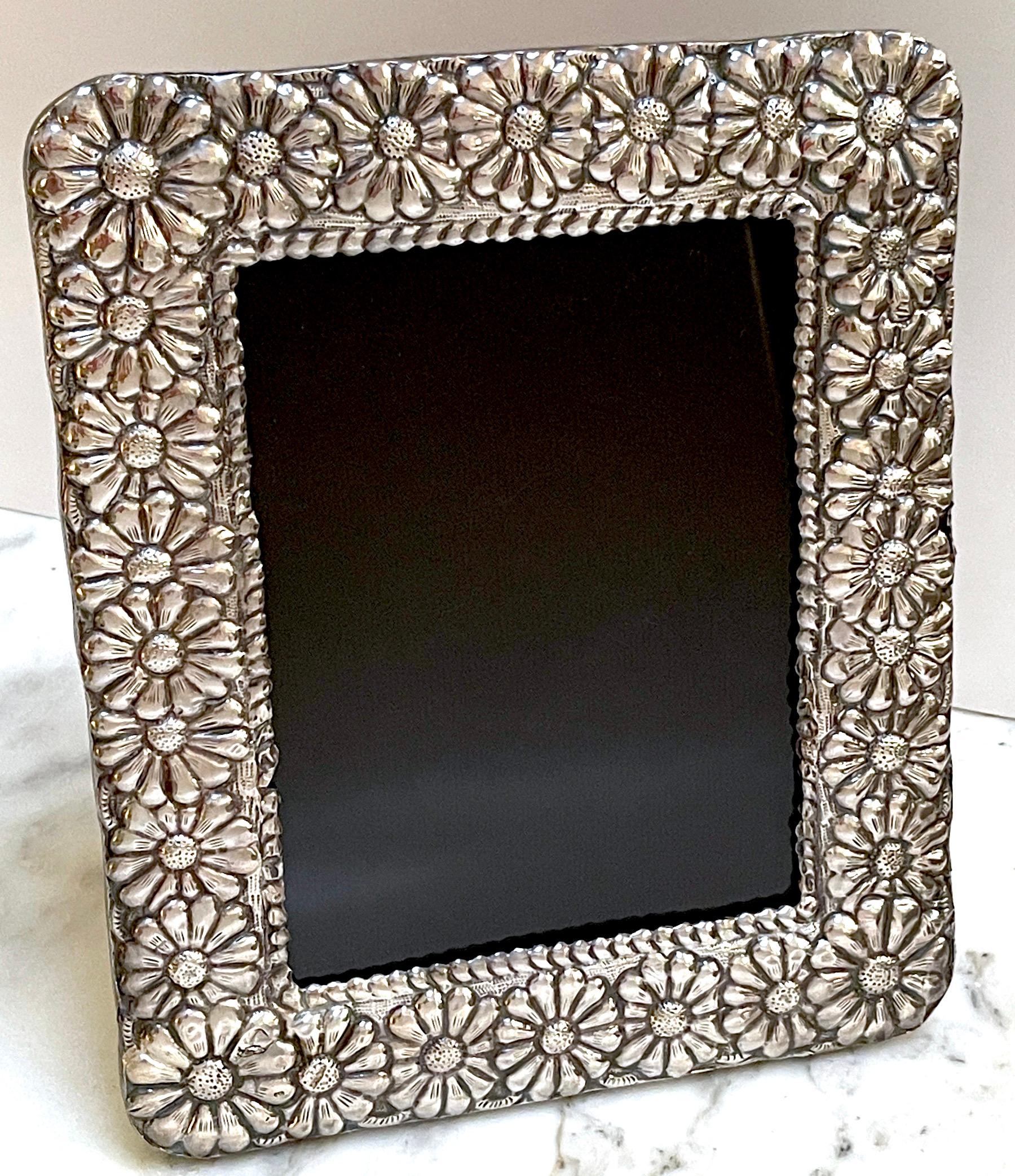 Modern Sterling Taxco School Picture Frame
Mexico, circa 1960s
With a continuous surround of repoused flower-heads 
Supported on a beautifully crafted hardwood backing with inset glass front.
Stamped .950 lower left corner. 
This frame will hold a