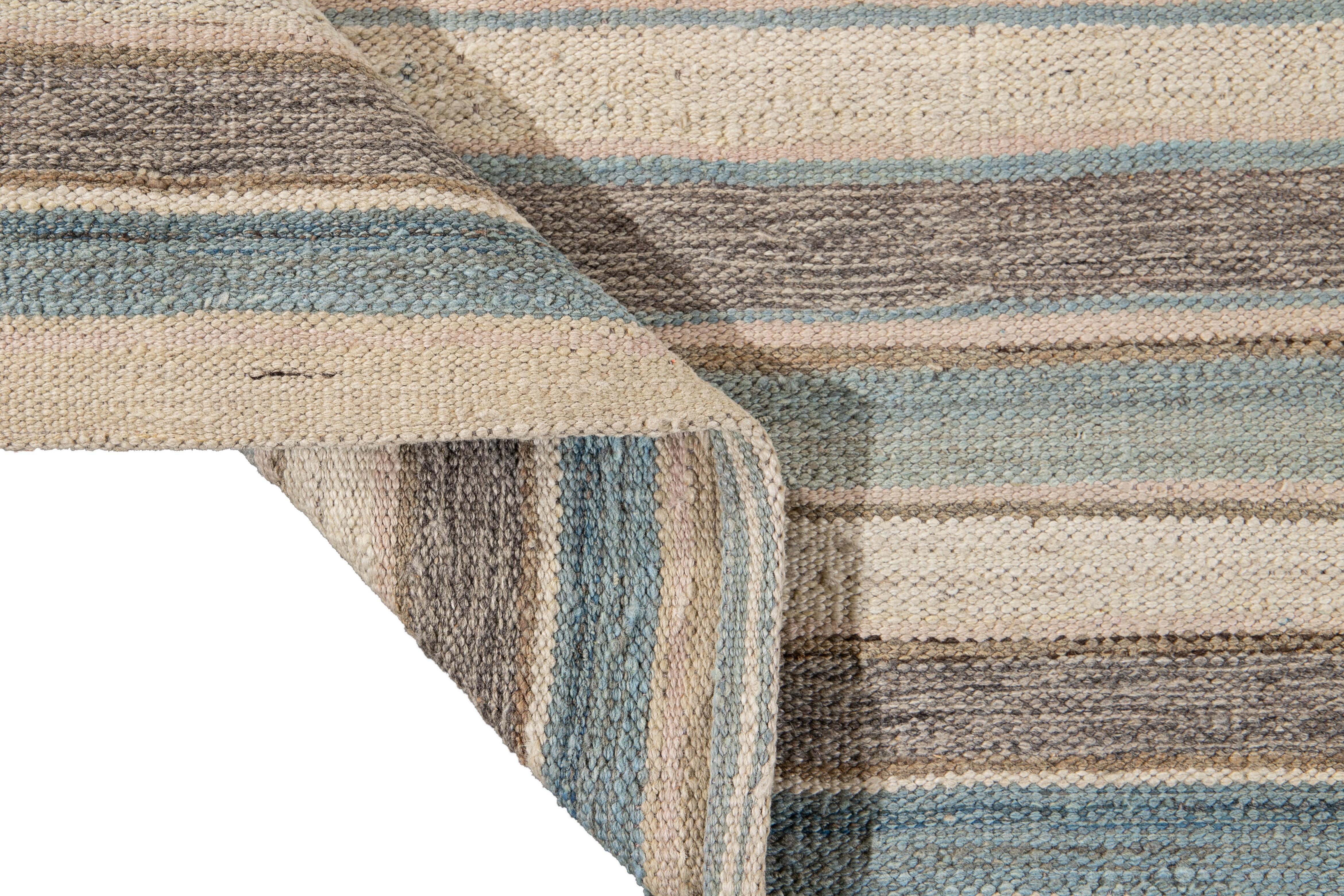 Beautiful modern flat-weave Kilim hand knotted wool rug. This rug has a field of beige, blue, and brown color in a gorgeous all-over geometric stripe design.

This rug measures 8'6