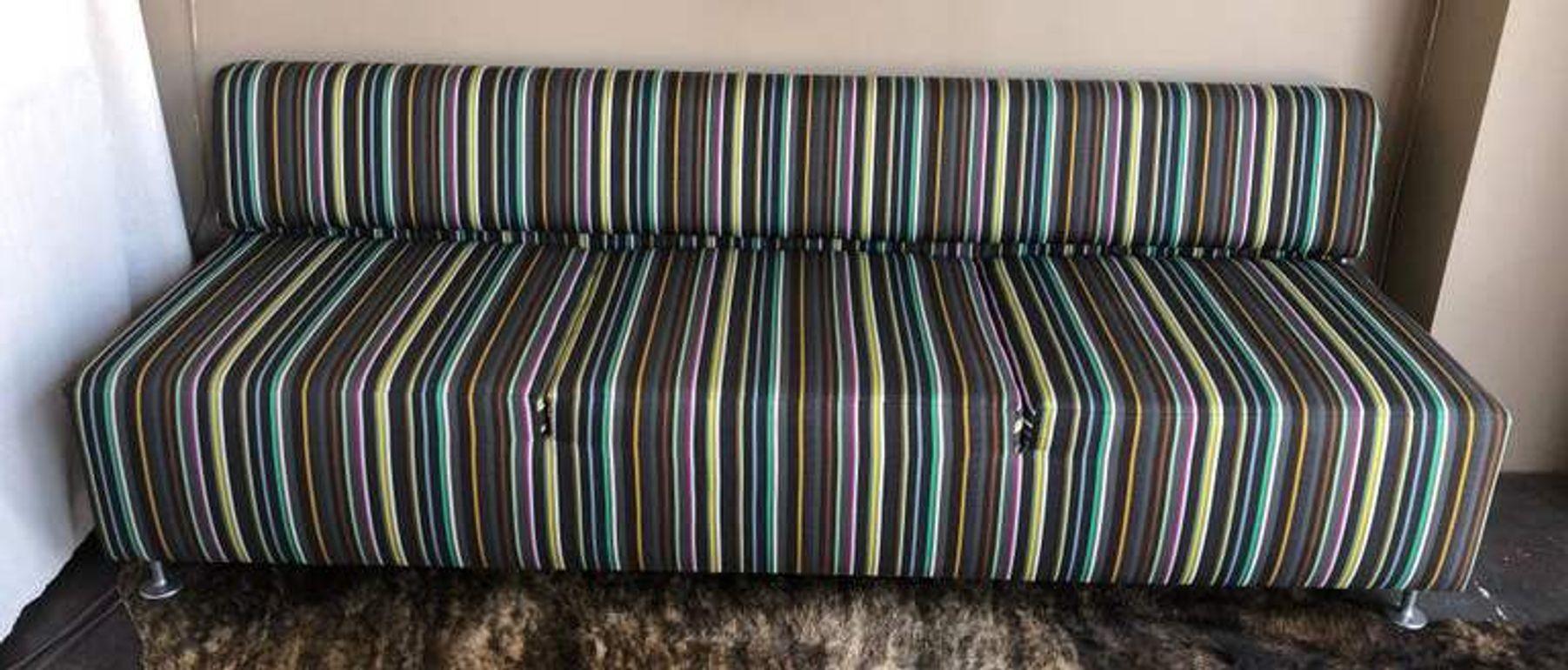 A stylish modern low back sofa upholstered in vibrant multi-color striped fabric, offering a playful yet sophisticated aesthetic. Designed with clean, minimalist lines and a compact profile, this 2005 piece brings contemporary charm to any living
