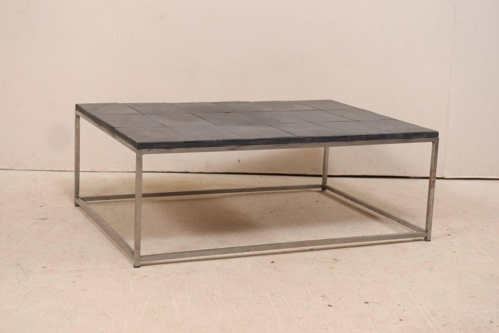 A modern style custom coffee table with slate tiled top. This rectangular-shaped coffee table features a slate tile top set into a custom silver metal frame, with four straight legs and braced with box stretchers at the feet. This slate topped