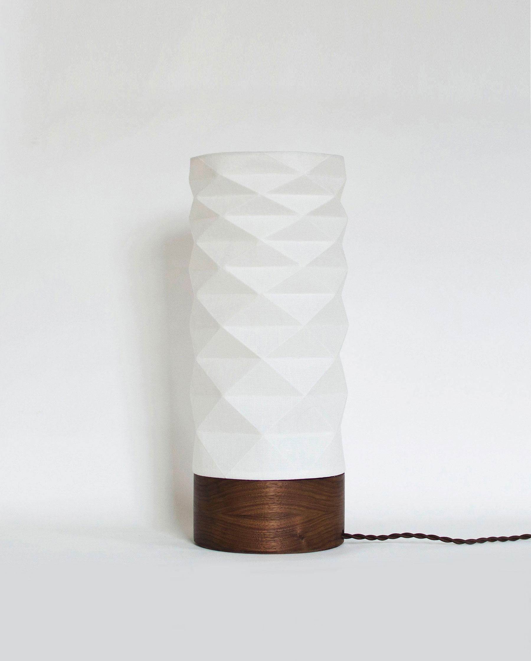 Cette lampe de table artisanale apportera à votre intérieur une pièce fonctionnelle unique et moderne. L'abat-jour inspiré de l'origami est fabriqué en tissu de lin laminé, ce qui permet d'obtenir une lumière ambiante à la fois claire et douce, tout