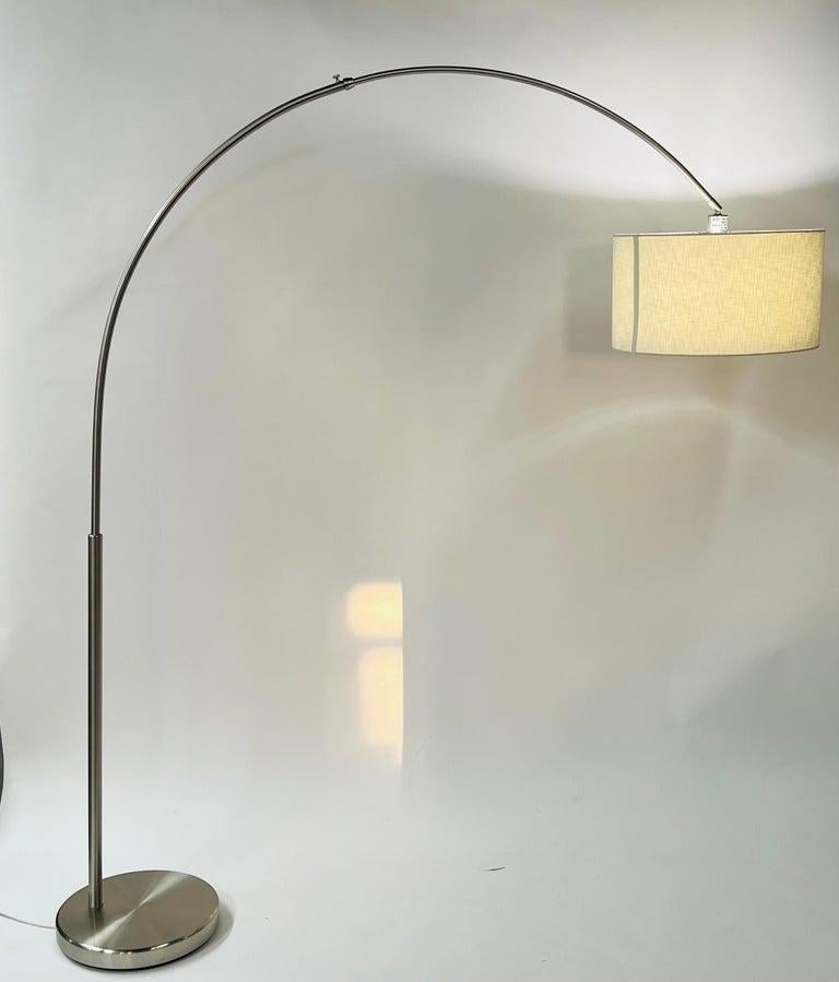 A large modern tall adjustable arched floor lamp with double drum shade. The lamp base is made of metal chrome and the shade is made of fabric in off-white. The light is adjustable creating a soft atmosphere as well as a bright one for more light.