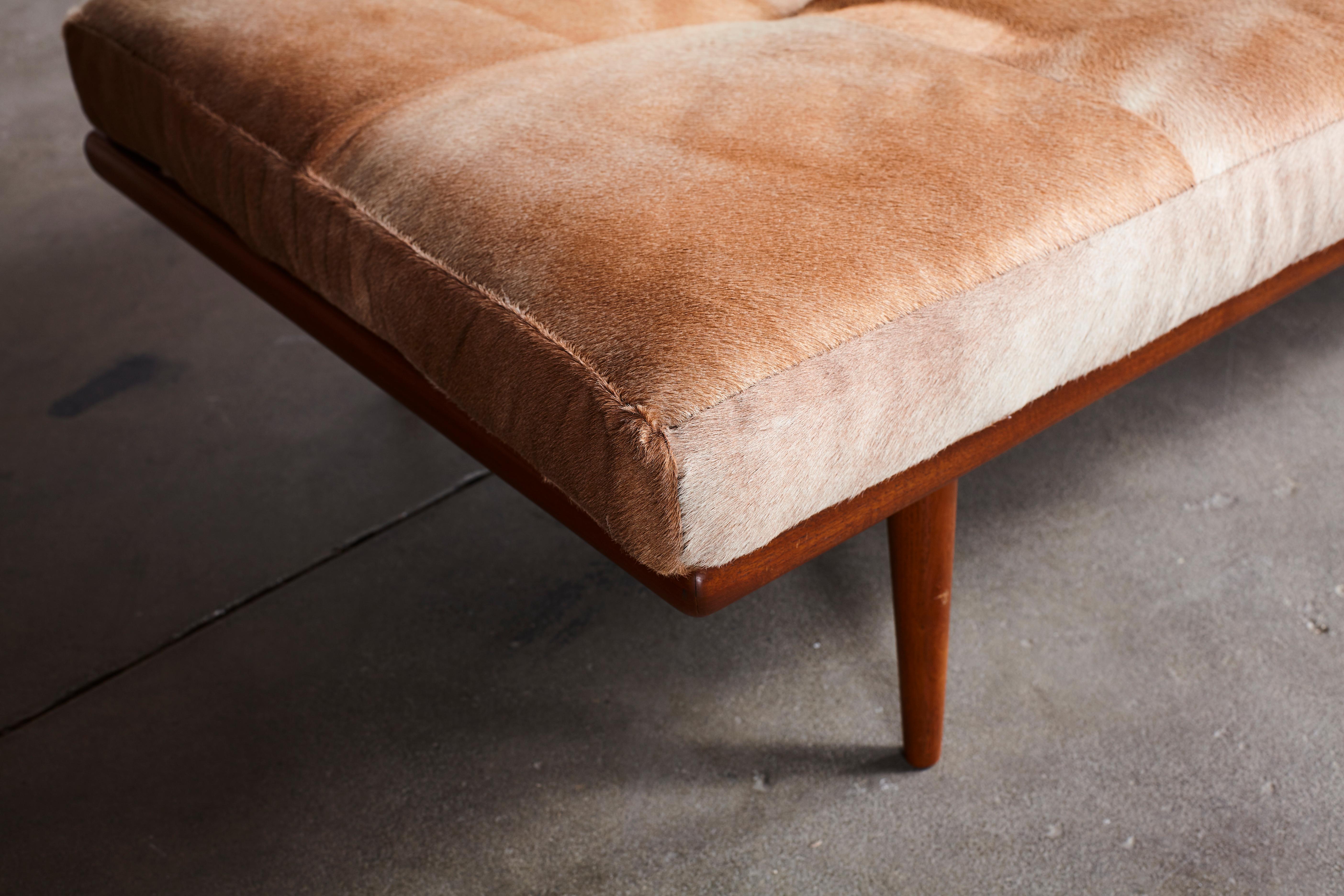 Modern teak bench with tapered legs, upholstered in a quilted horse hide cushion.