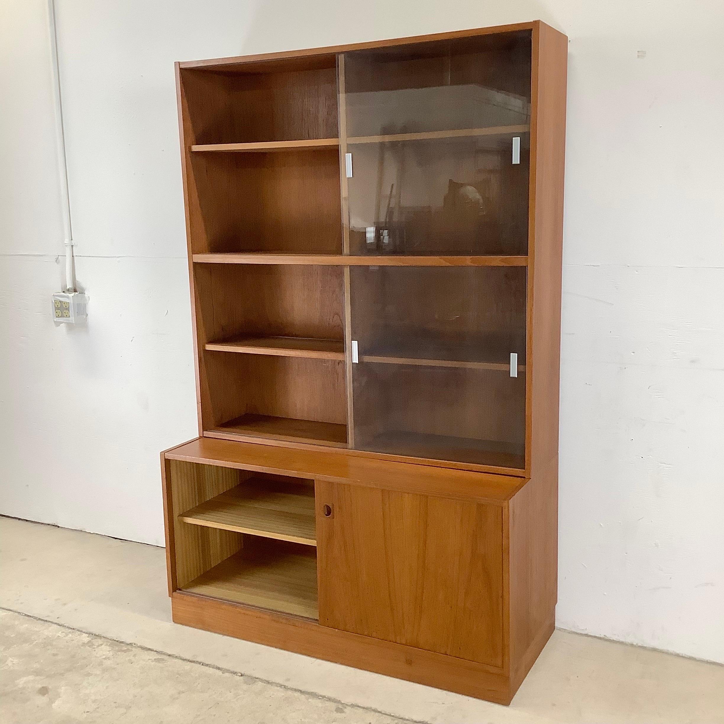 This substantial two piece teak bookcase features a sliding glass front display topper with adjustable shelves paired with a sliding teak door storage cabinet as a base. The two piece set offers the perfect mix of showroom style display with lower