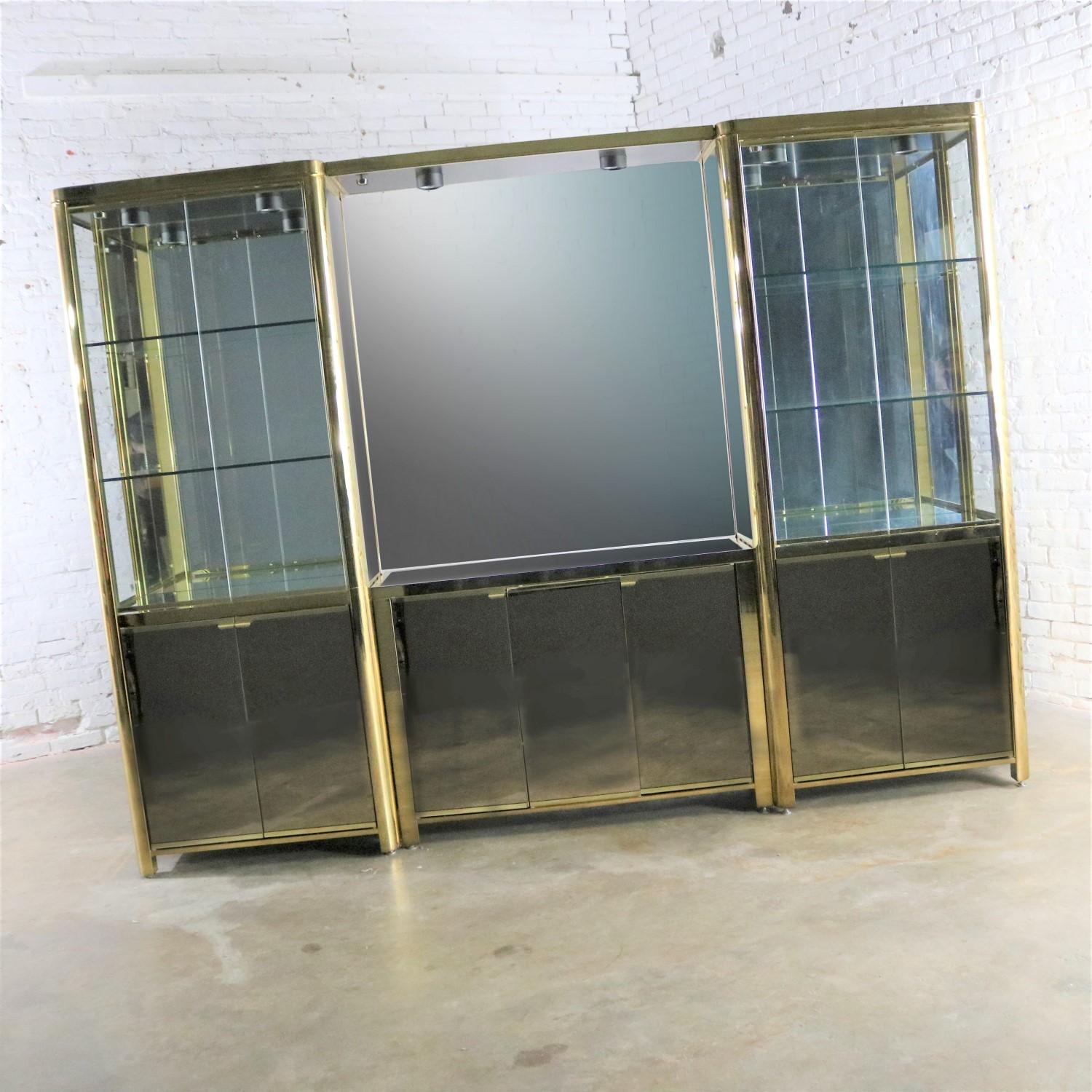 Magnificent modern triple wide lighted vitrine or display cabinet in brass plated metal, glass, and mirror. Unmarked but similar in style and quality of Ello or Mastercraft. Each piece is finished on both side so they are each able to stand on their