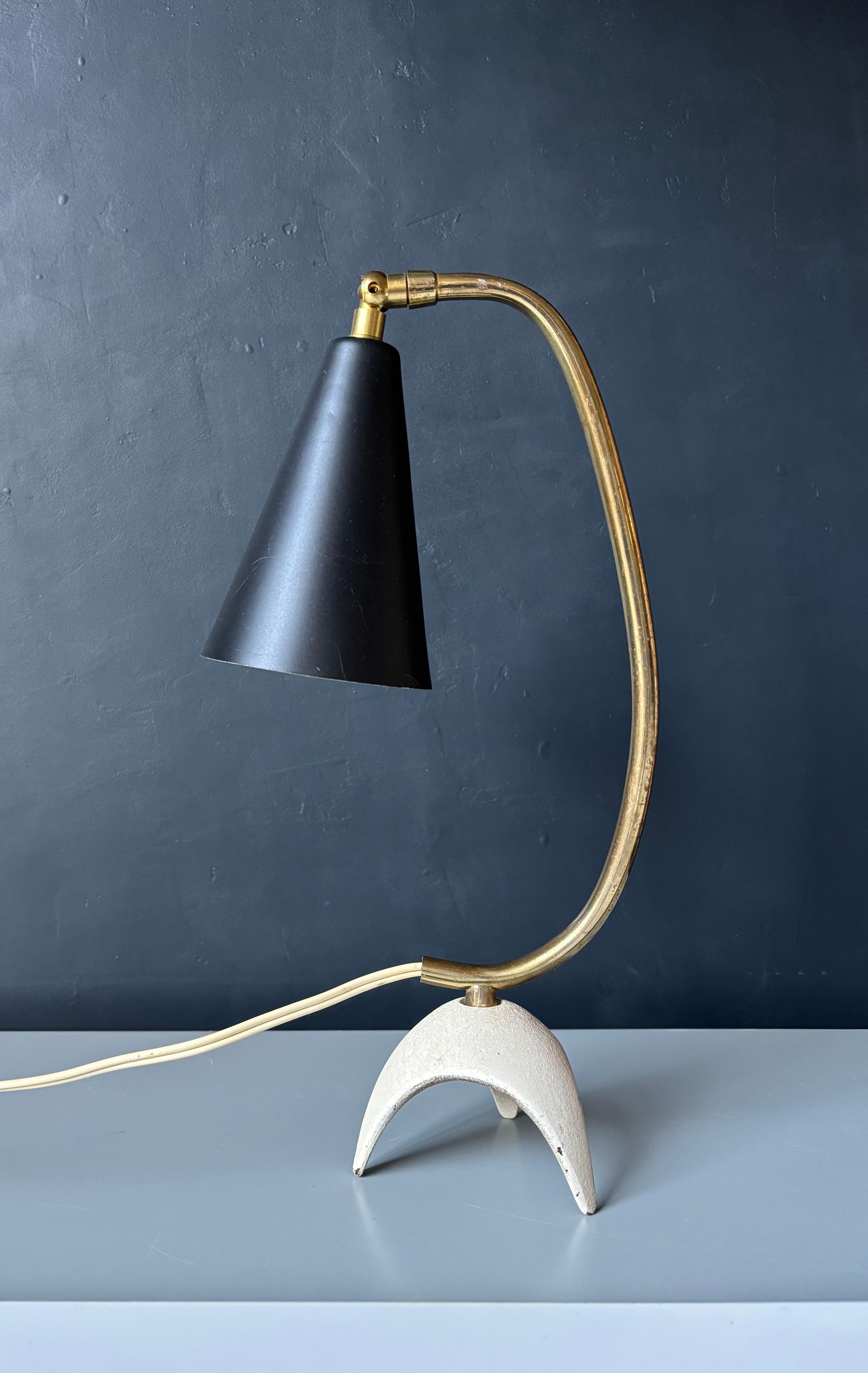 Lampe de table simple et moderne du milieu du siècle avec abat-jour conique en métal ajustable noir mat sur une monture en laiton à col de cygne légèrement incliné et un pied tripode rustique de couleur sable. 
Câblé pour une utilisation dans l'UE