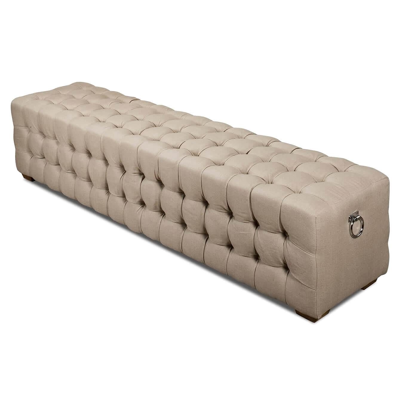 A modern tufted upholstered bench. This bench is covered in luxurious beige linen with a tufted design on its tops and sides. It sits on oak legs in a natural finish and has two silver ring handles on each end.

The neutral color and the timeless