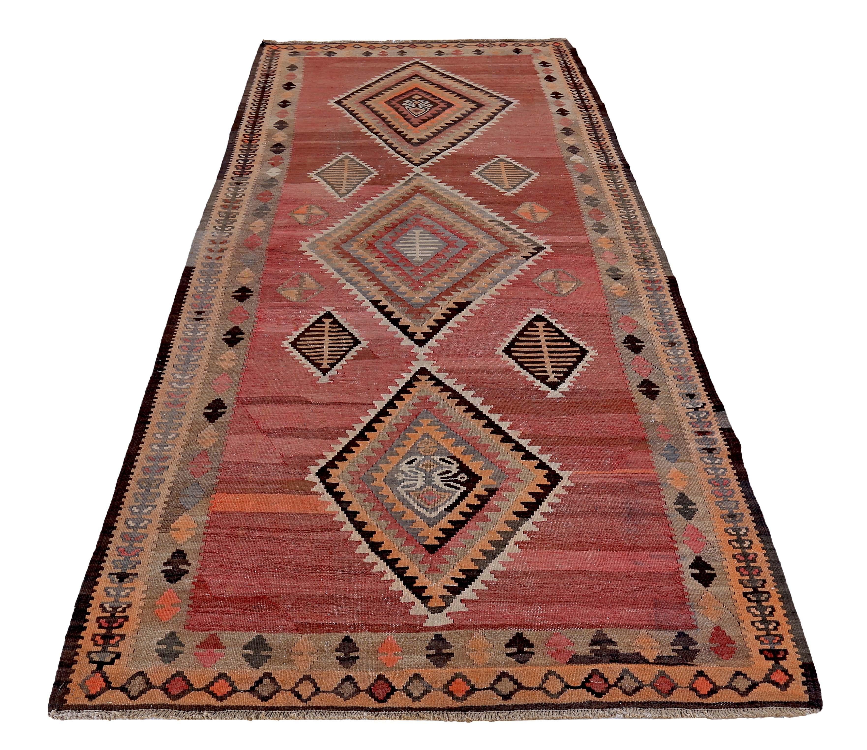 Turkish rug handwoven from the finest sheep’s wool and colored with all-natural vegetable dyes that are safe for humans and pets. It’s a traditional Kilim flat-weave design featuring black, brown and red tribal diamond patterns on an orange field.