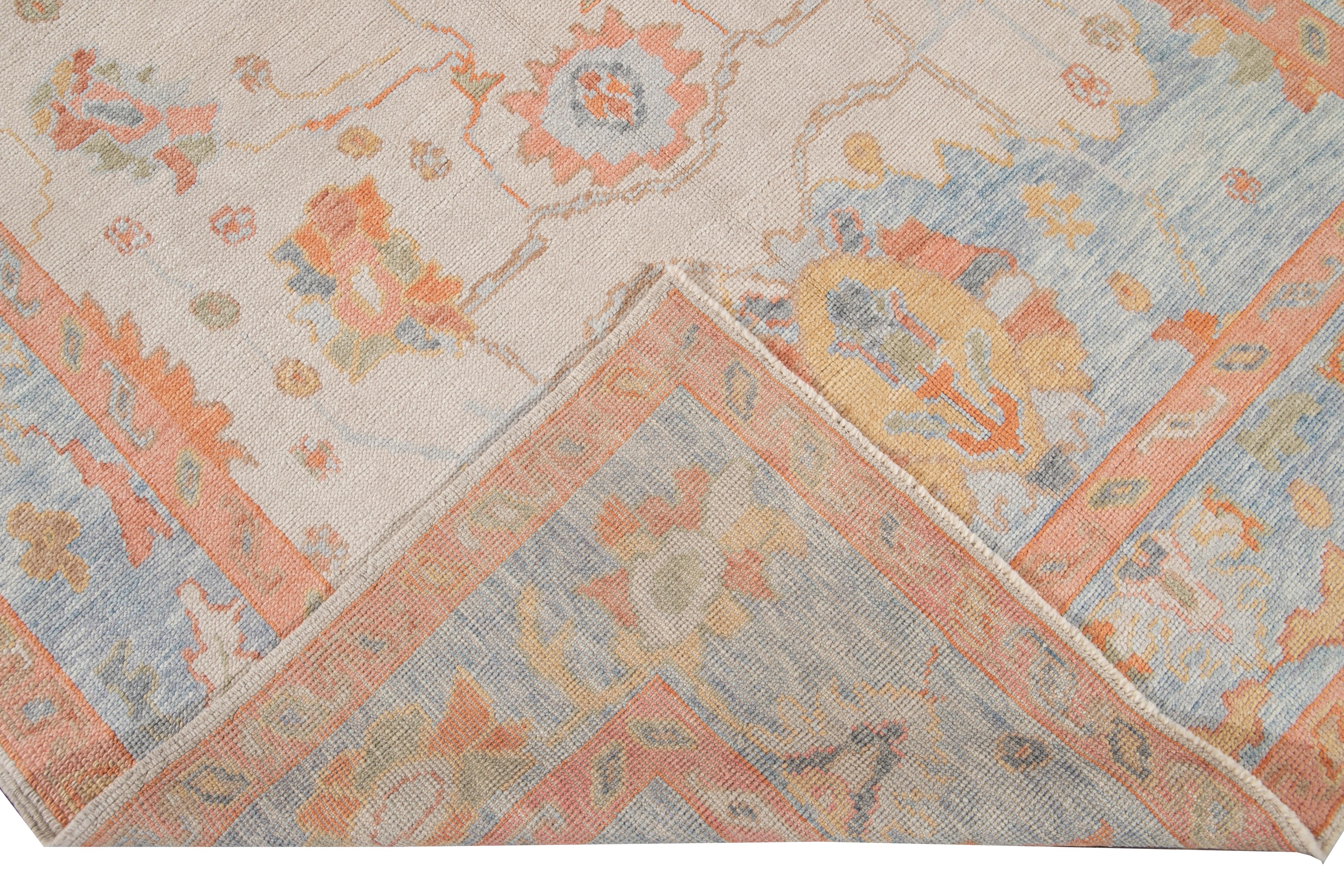 Beautiful modern Oushak hand knotted wool rug with a beige field. This Oushak rug has a blue and orange frame and accents of orange, green, and peach all-over a gorgeous geometric floral design.

This rug measures: 6'3
