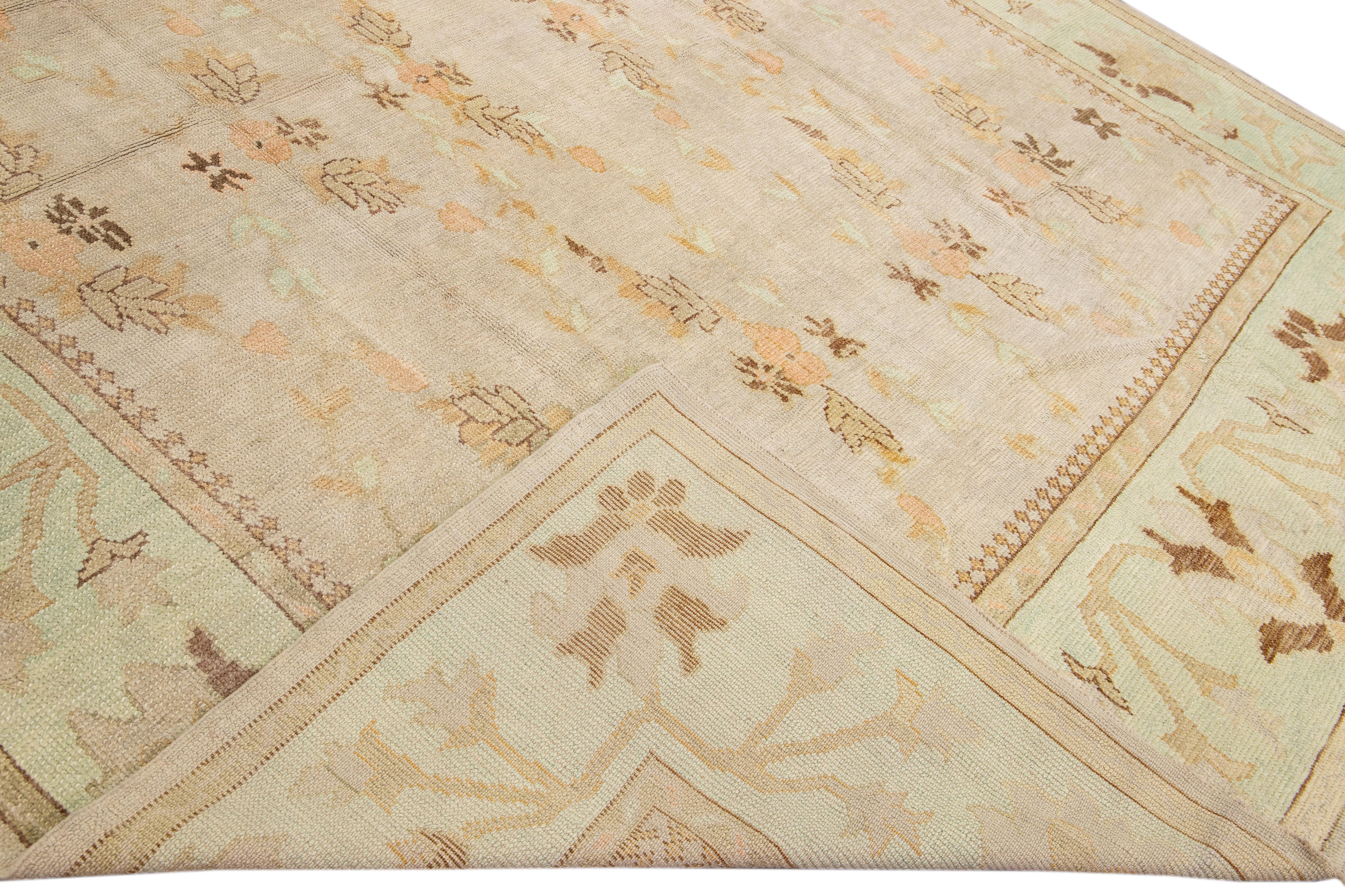 Beautiful modern oushak hand-knotted wool rug with a beige field. This Turkish piece has a green-designed frame and peach and brown accents in a gorgeous all-over geometric floral Motif.

This rug measures: 10' x 14'9