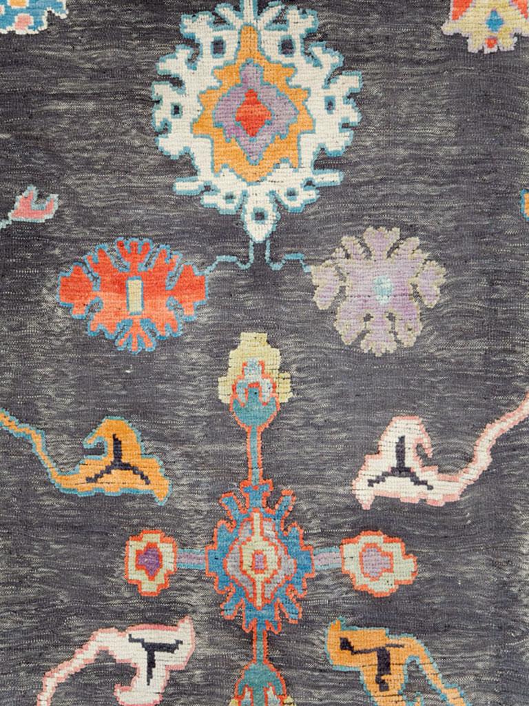 A contemporary Oushak carpet from the 21st century with a souf design. Souf consists of a flat-woven background (grey/charcoal in this field representation and light blue in the border) and raised piles to form the motifs (multicolored).
