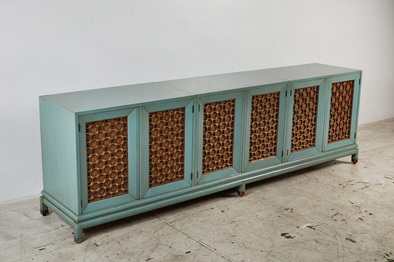 Modern turquoise-stained three-part side cabinet on separate stand.
Large contemporary painted console or cabinet with beautiful brass inset grilles, backed with caning, and brass-capped feet in the ever-so-popular Hollywood Regency style. This