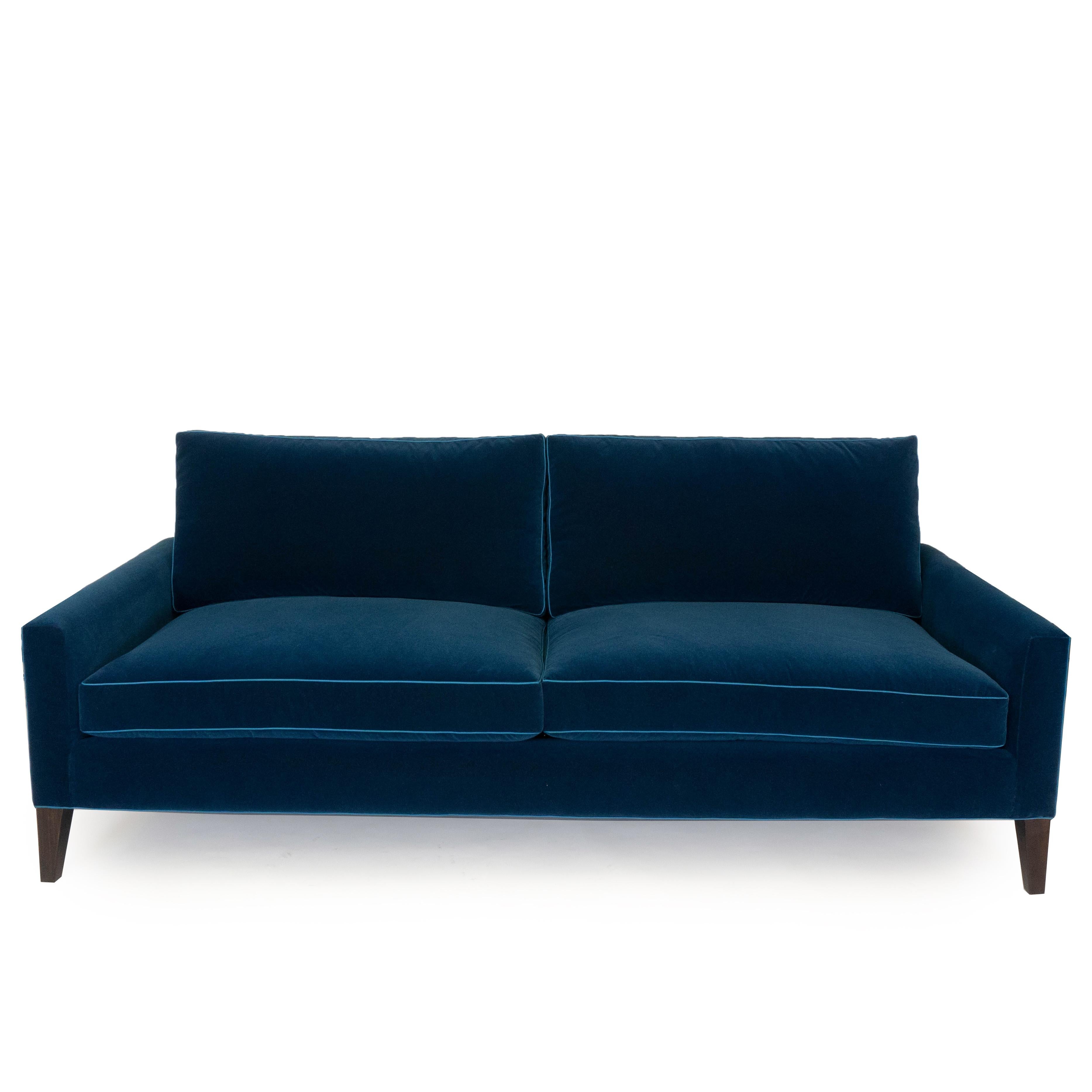 Our modern two cushion sofa is upholstered in a dark blue velvet with an infinity cotton feel and features a light blue polyester trim. This sofa is handmade with poplar wood and finished with a dark walnut painted leg. The cushions are made with 5