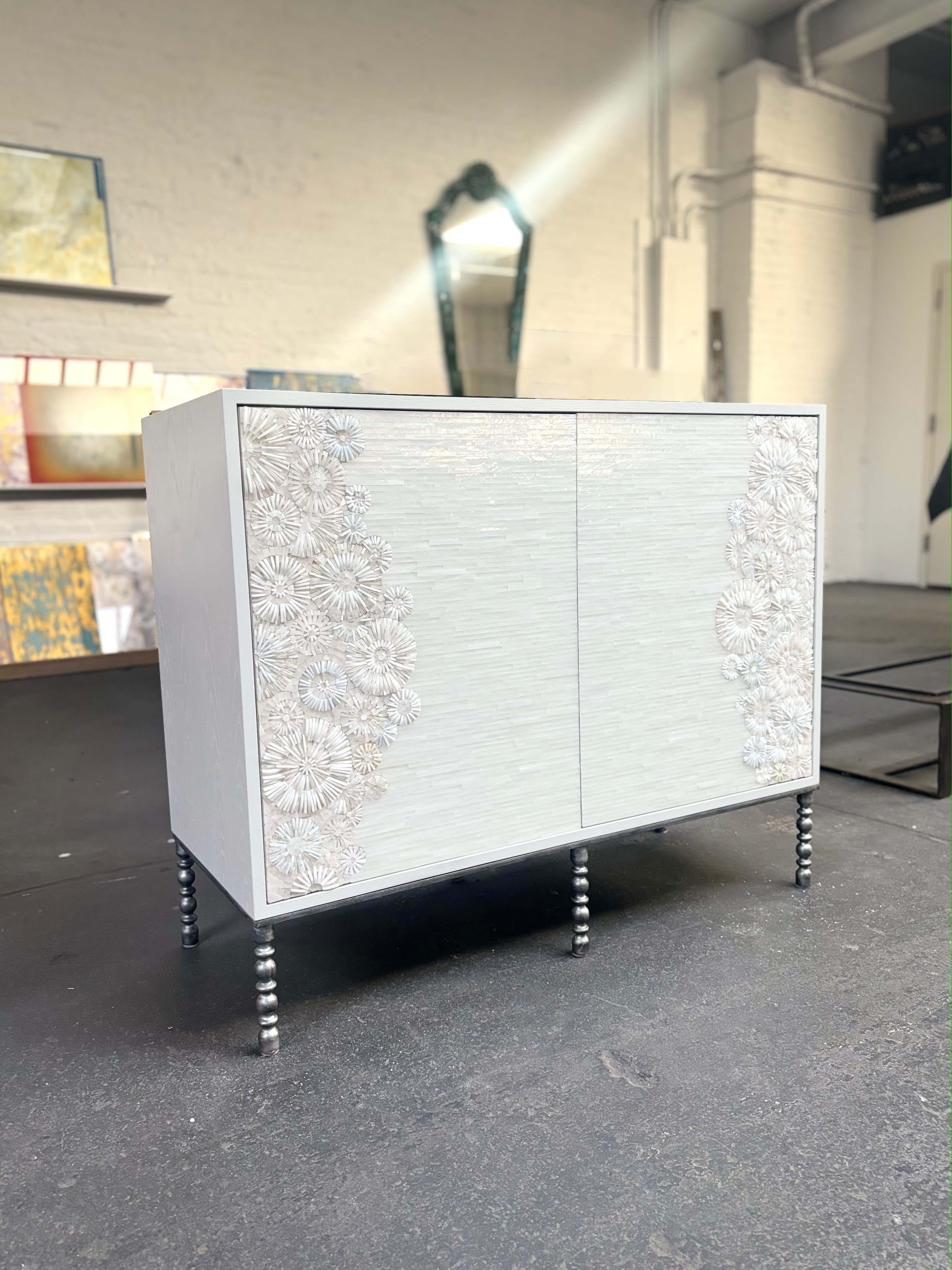 Il Buffet moderno a due ante Blossom con base in stile vintage di Ercole Home ha un frontale a due ante, con finitura bianca su legno di quercia. Il mosaico di vetro tagliato a mano in varie tonalità di vetro bianco e avorio decora la superficie con