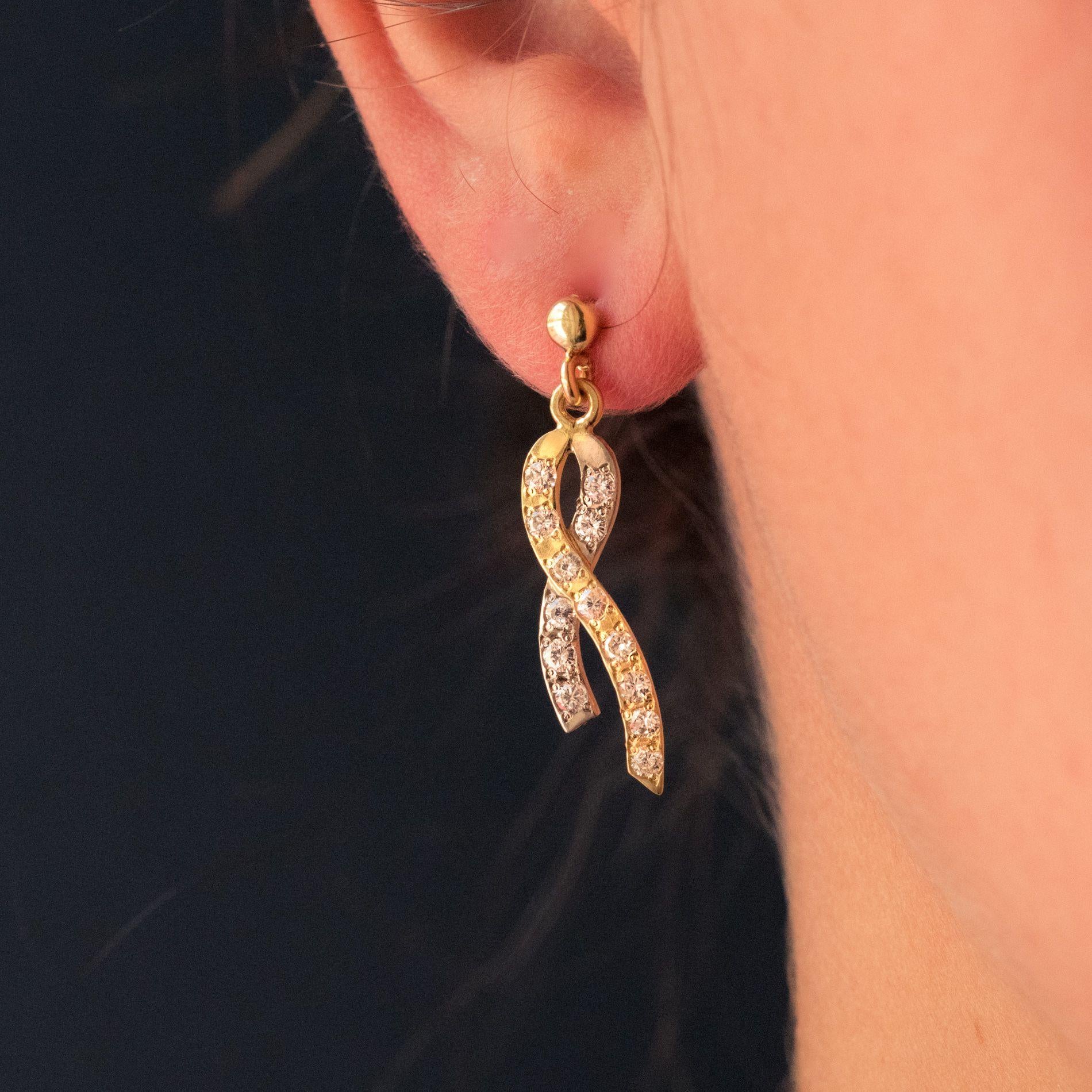 For pierced ears.
Earrings in 18 karat yellow and white gold.
In the shape of a ribbon with one side in yellow gold and the other in white gold, each earring is set with 13 brilliant- cut diamonds on the front. This pattern is supported by a flat