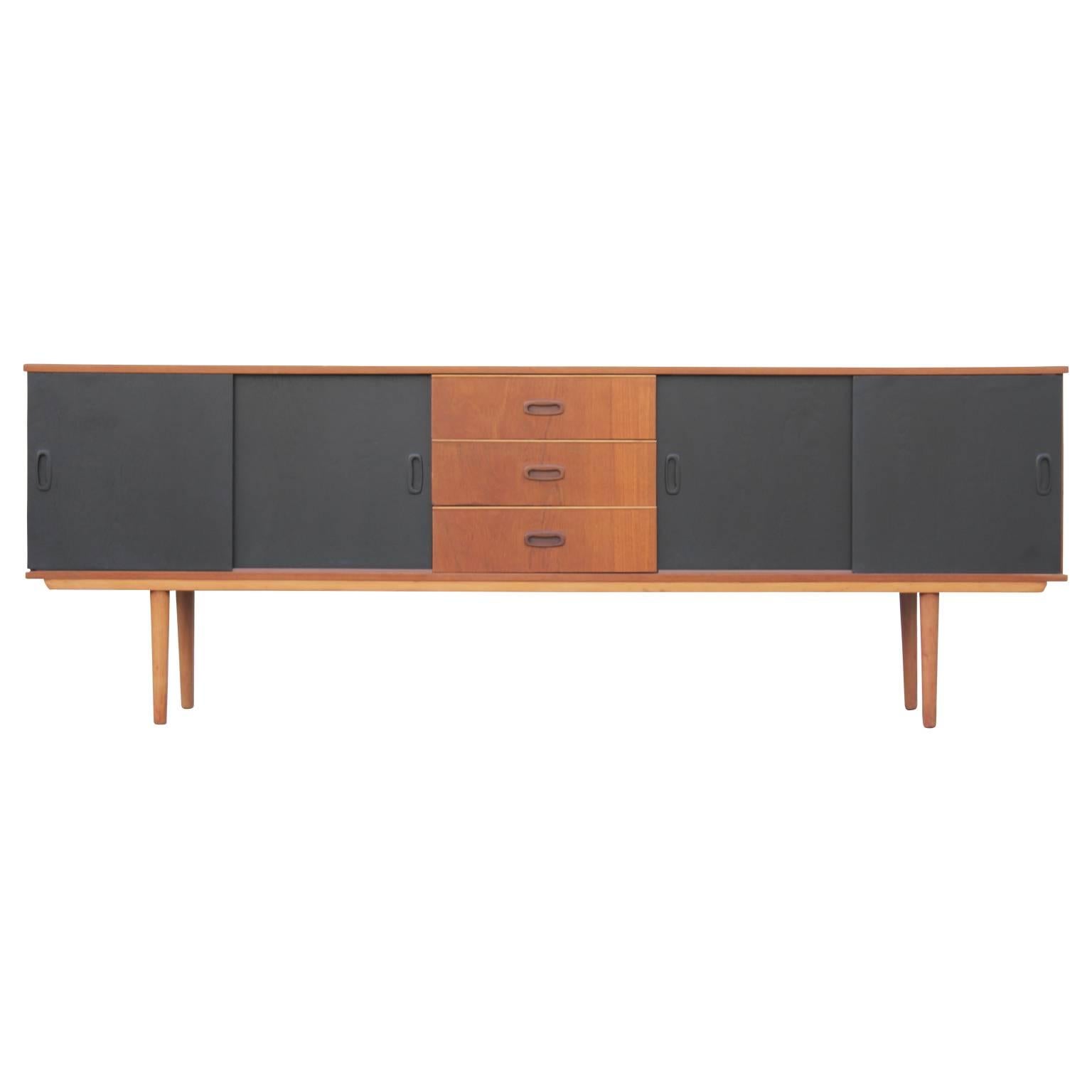 Mid-Century Modern two-tone credenza or side board with three drawers and sliding doors. The panel on the left opens to reveal an open cabinet space while the panel on the right opens to reveal a single shelf.