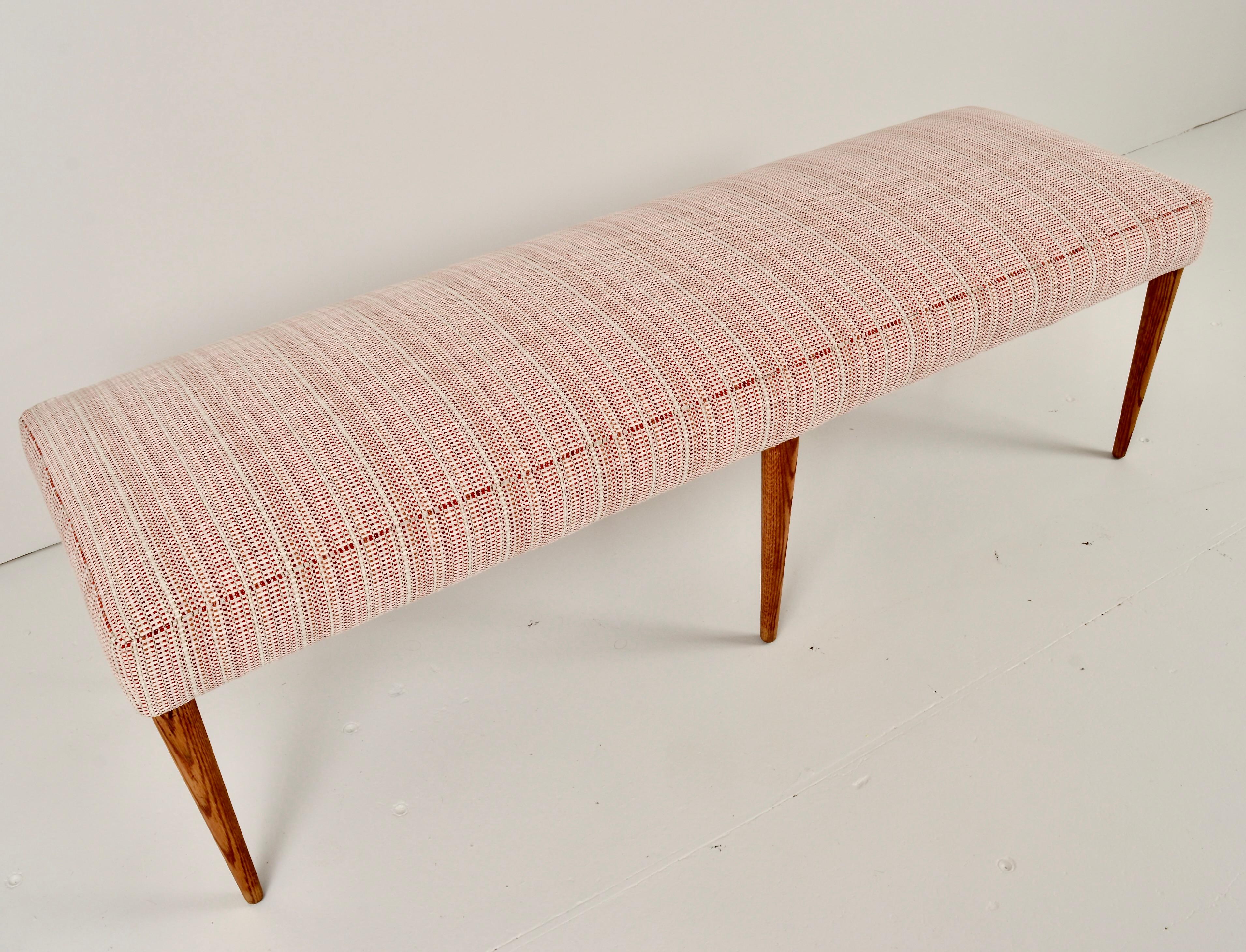 Six  wonderfully tapered oak legs on this long bench. At 60 inches a very useful size. This vintage bench has been completely reupholstered in a nubby striped fabric in pink and rose tones. Very sturdy and in excellent condition.