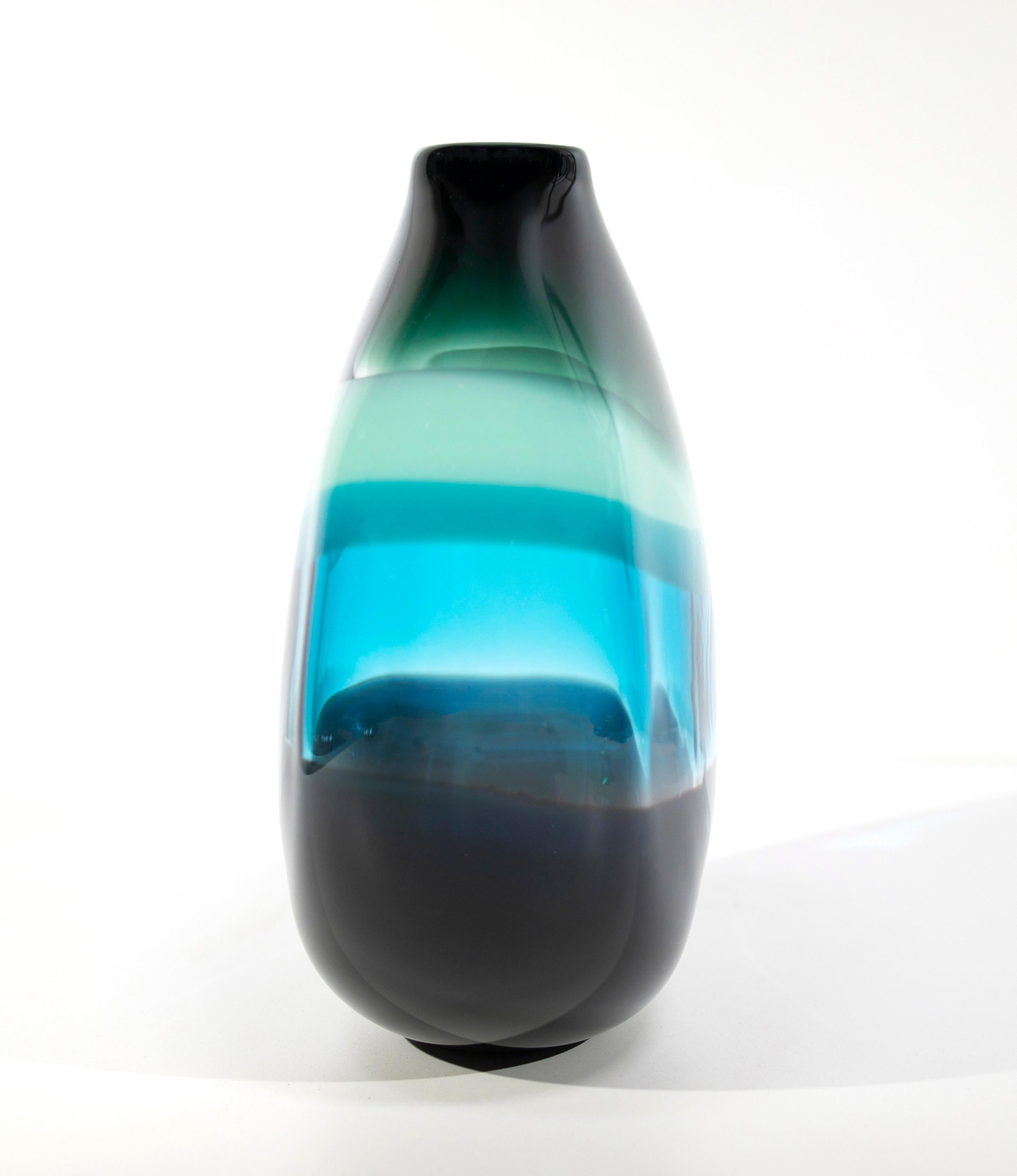 Aqua banded vase. Inspired by the rich hues and topography of Southern California, alternating layers of opaque and transparent colors are applied to clear glass. New colors are formed by overlaps, adding depth to the pieces. Simple shapes