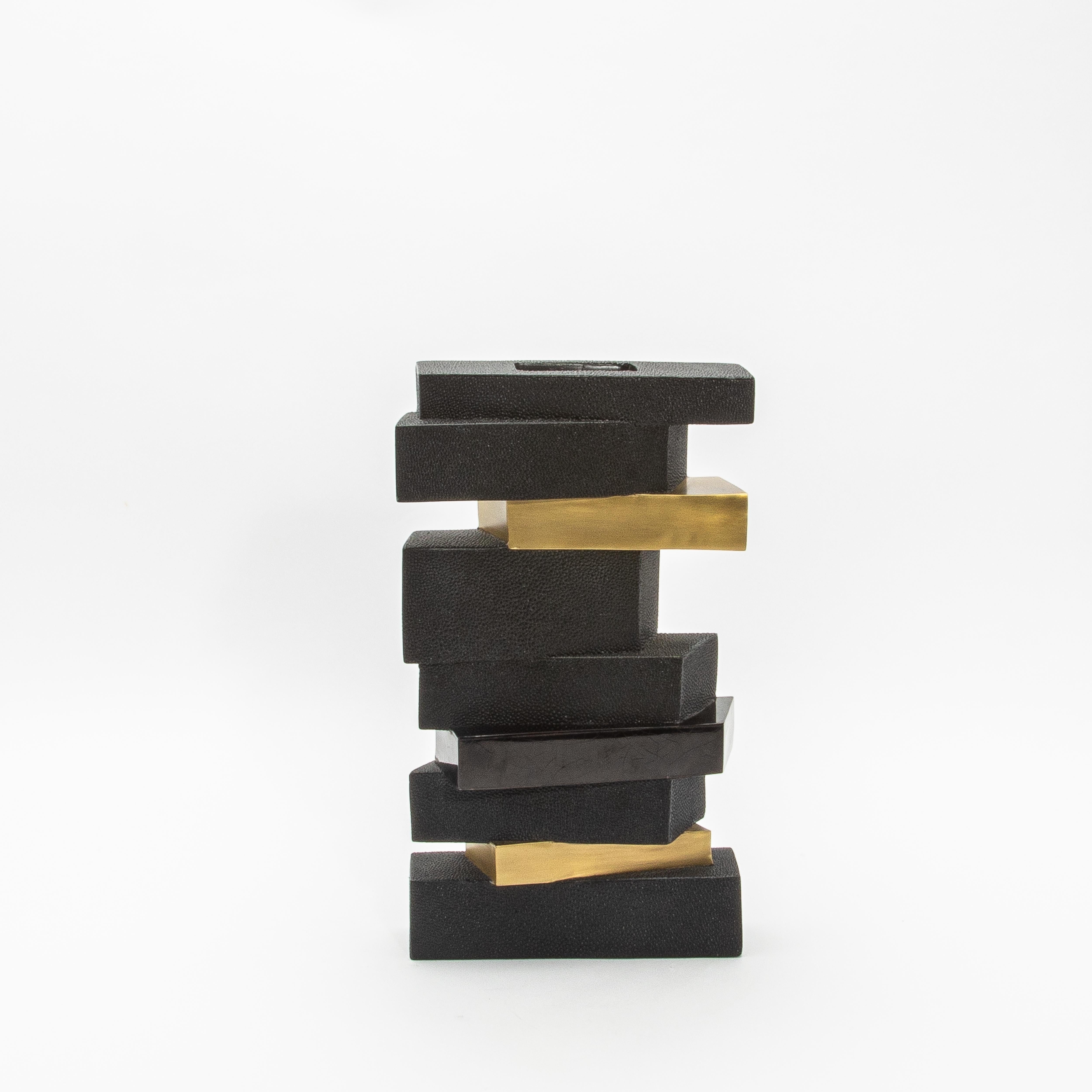 The “Bullion Confection Vase” is bold and sculptural an captivates with its layered geometric design, exuding an artful interplay of textures and materials. Its stacked formation combines tactile black shagreen blocks with sleek, polished brass