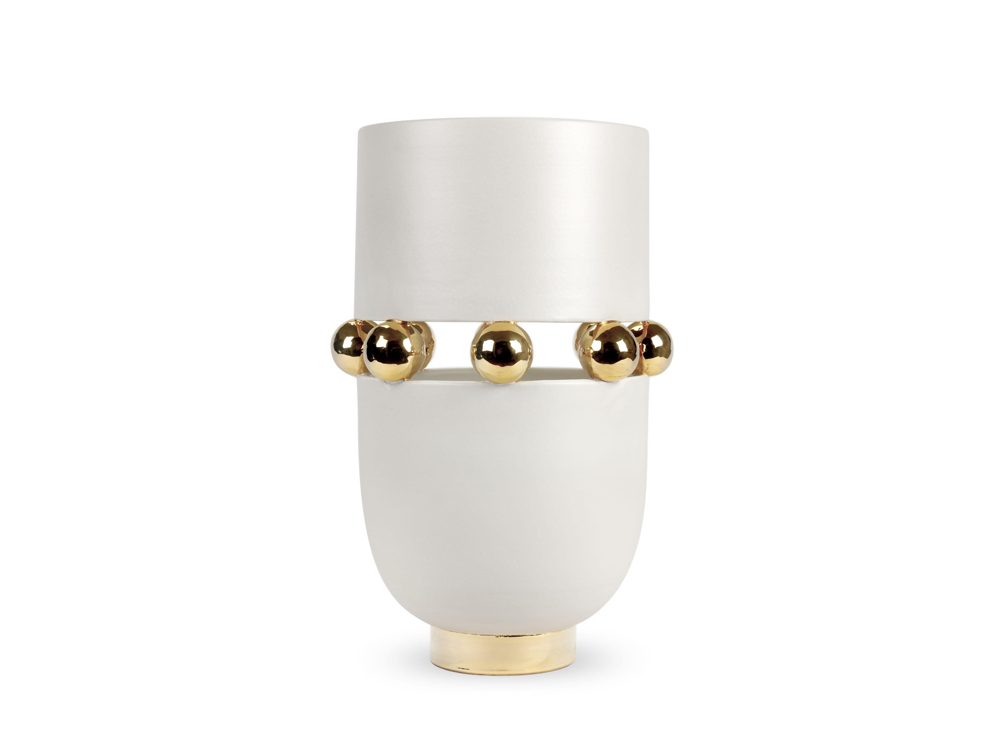 Elegant warm white vase with a matte finishing, alternating with reflective surfaces embellished with 24Kt gold luster. This technique sees ceramics to undergo three cooking phases: the last one, called third firing, lets the gold luster release its