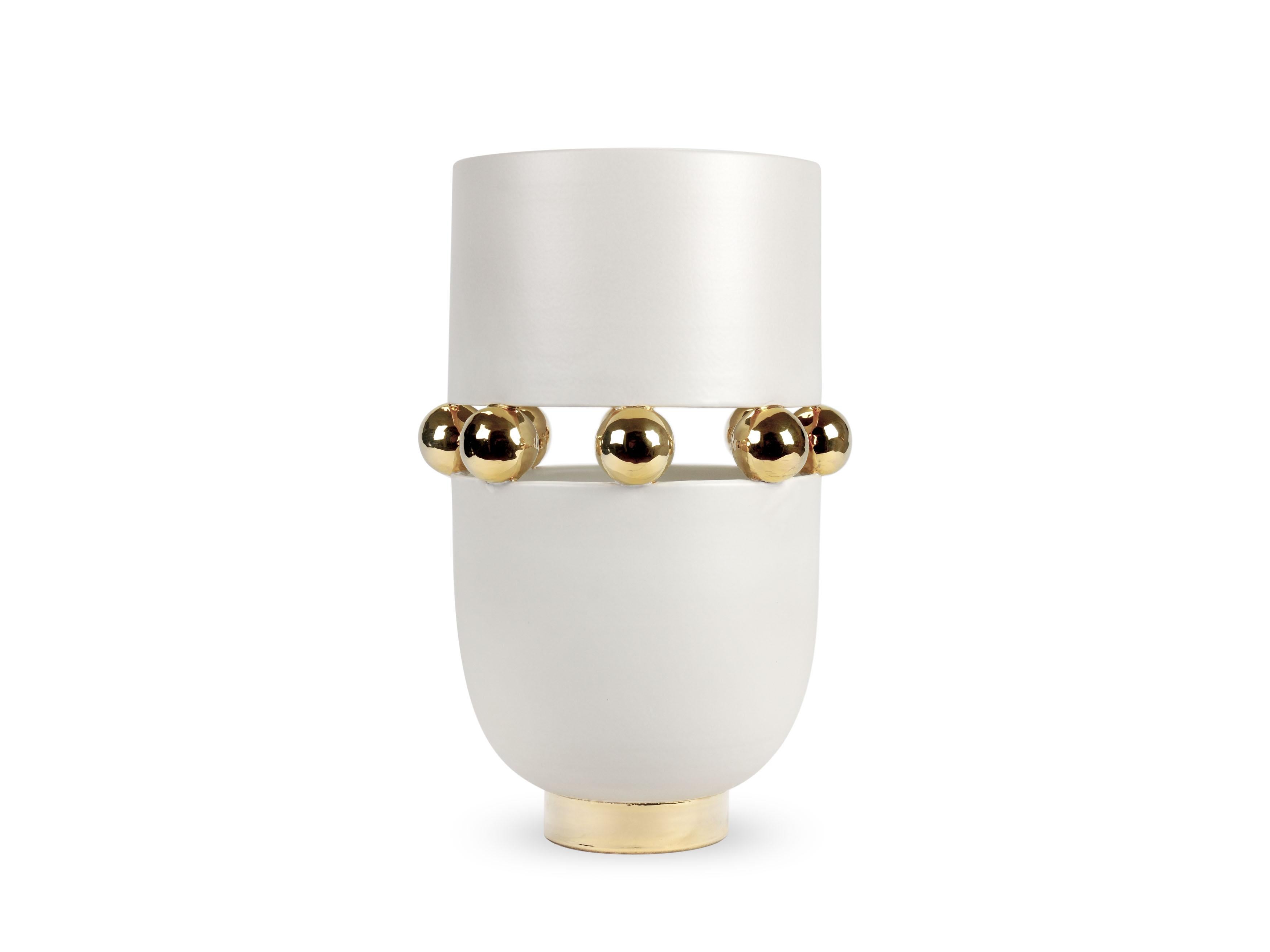 Elegante vaso bianco caldo con finitura opaca, alternato a superfici riflettenti impreziosite dalla lucentezza dell'oro 24Kt. Questa tecnica prevede che la ceramica venga sottoposta a tre fasi di cottura: l'ultima, chiamata terza cottura, permette