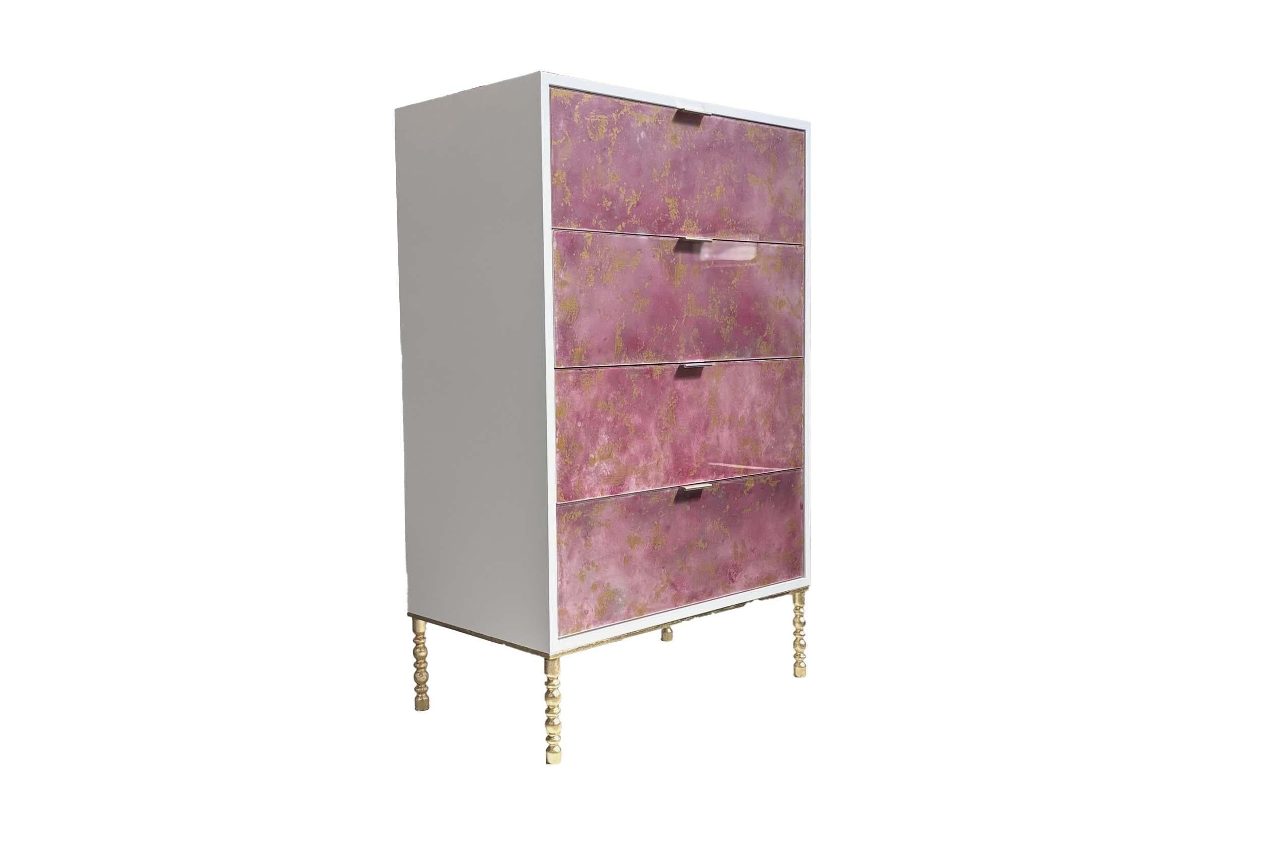 La Cómoda de cuatro cajones Fresco veneciano fucsia y dorado presenta un acabado de madera lacada en blanco con frentes de cajones en cristal Fresco veneciano pintado a mano en fucsia y dorado. El arcón se asienta sobre una base de estilo vintage de