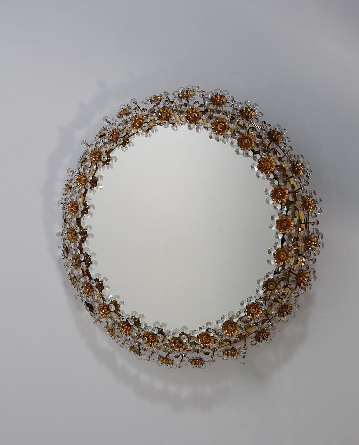 Modern vintage circular wall mirror with backlight from gilt brass and crystal flowers in earthen, gold and clear colors 1960s, Germany.
A stunning wall mirror in circular shape shows a frame decor with clear crystals and golden colored