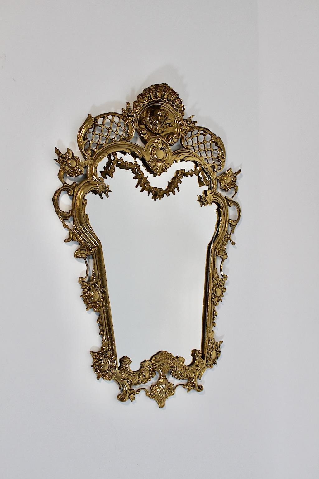 Modern brass vintage wall mirror in the style of baroque revival from cast brass and mirror glass Italy 1970s.
A stunning wall mirror from cast brass richly decorated with flower garlandes, angels and ornaments a a wonderful warm golden tone.
This