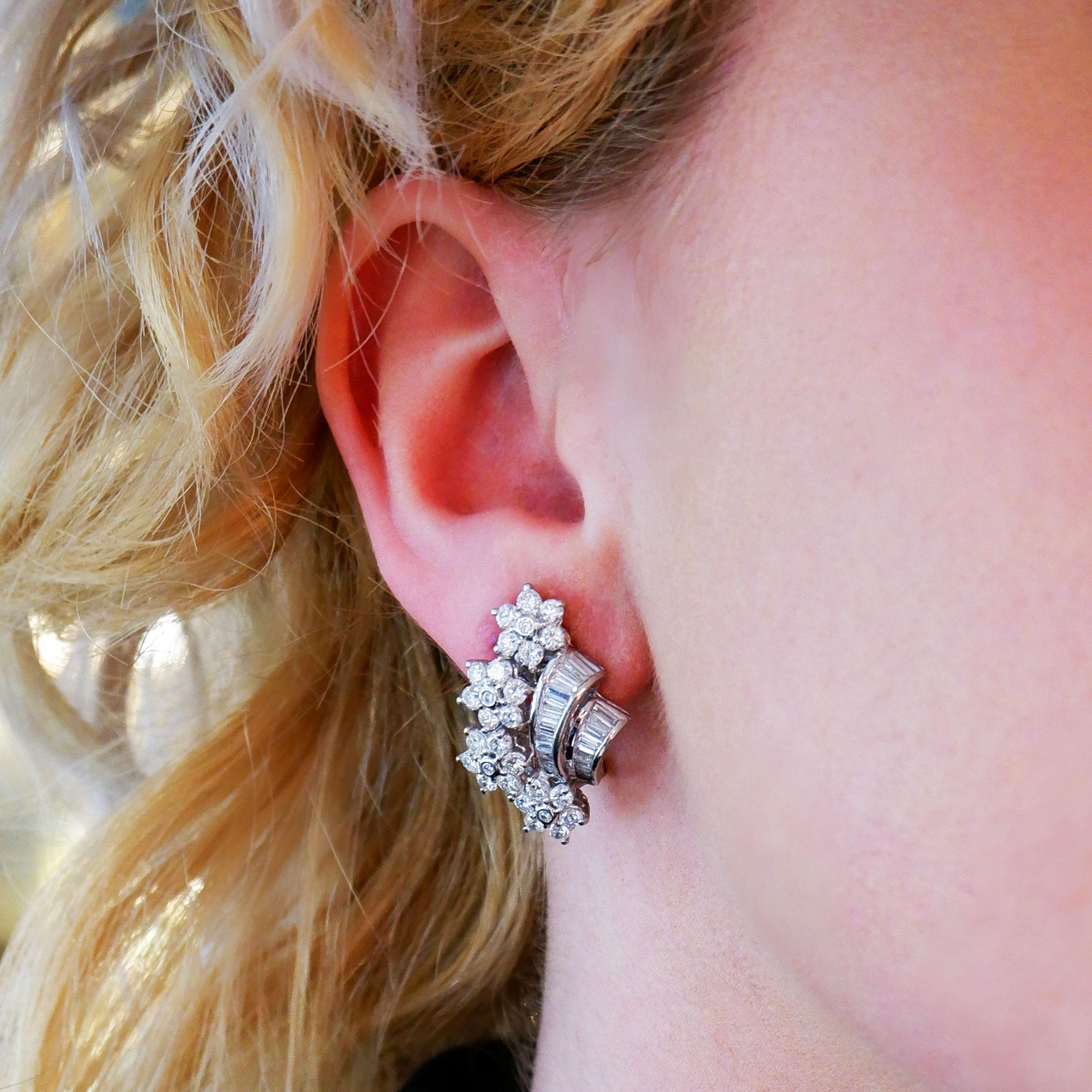 A pair of diamond vintage style flower spray clip-on earrings, featuring four flower clusters, with round brilliant-cut diamonds, the centre of each in a rub over setting, with the petals in claw basket settings, with two graduating rows of baguette