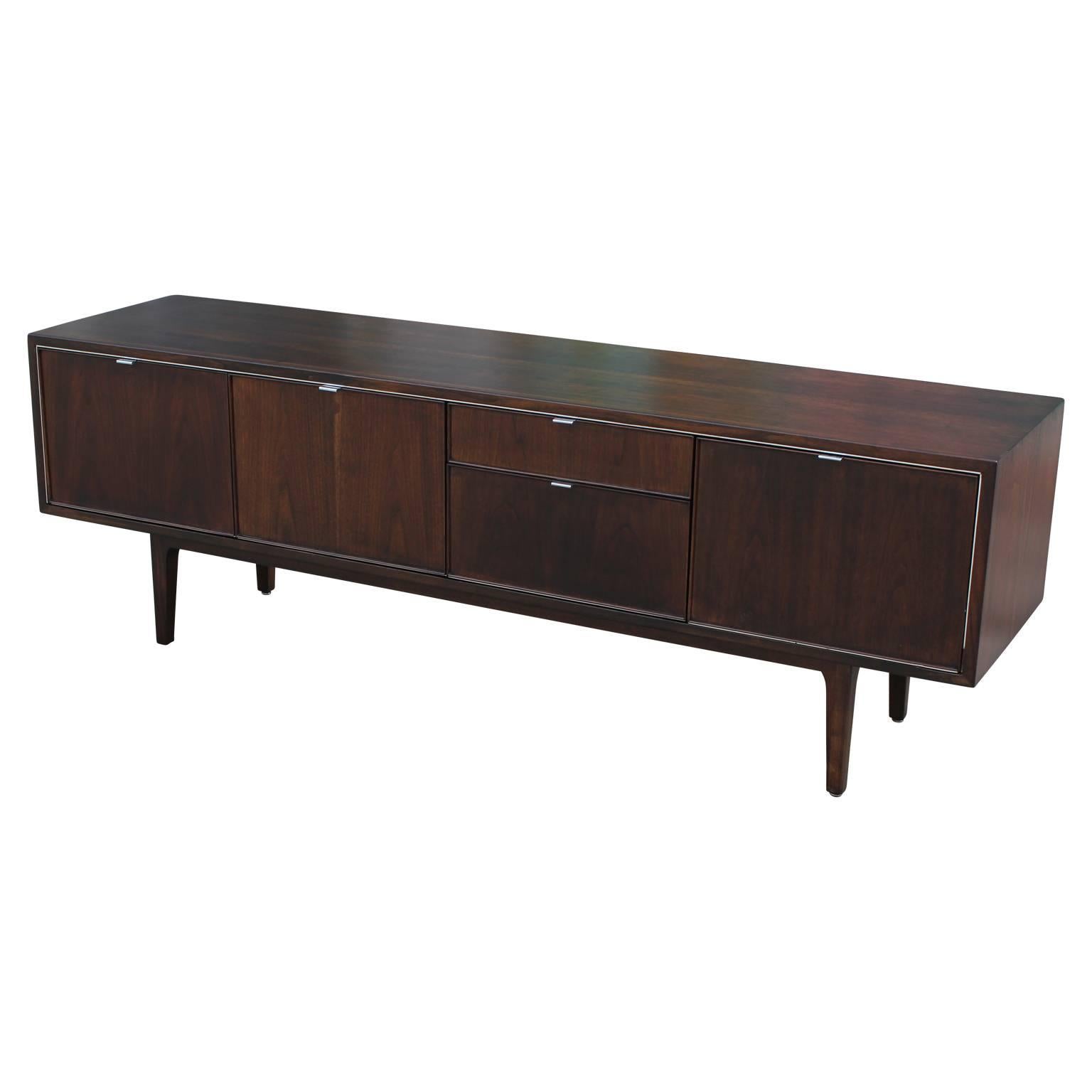 Gorgeous deep walnut credenza by Stow Davis. This sideboard features four drawers, perfect for storage and a drop door that opens to reveal a single adjustable shelf.