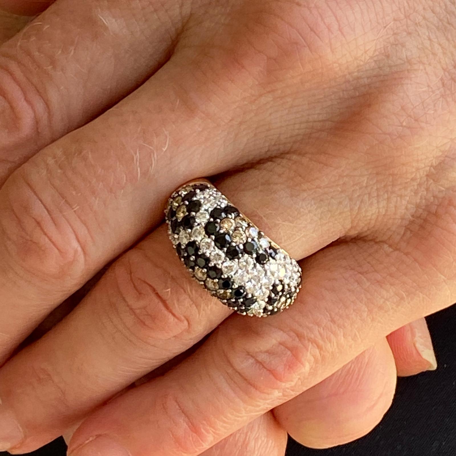 Stylish designer diamond band ring fashioned in 18 karat yellow gold. The round brilliant cut white diamonds weigh approximately 3.00 carat total weight and are graded G-H color and VS clarity. The champagne and black round brilliant cut diamonds