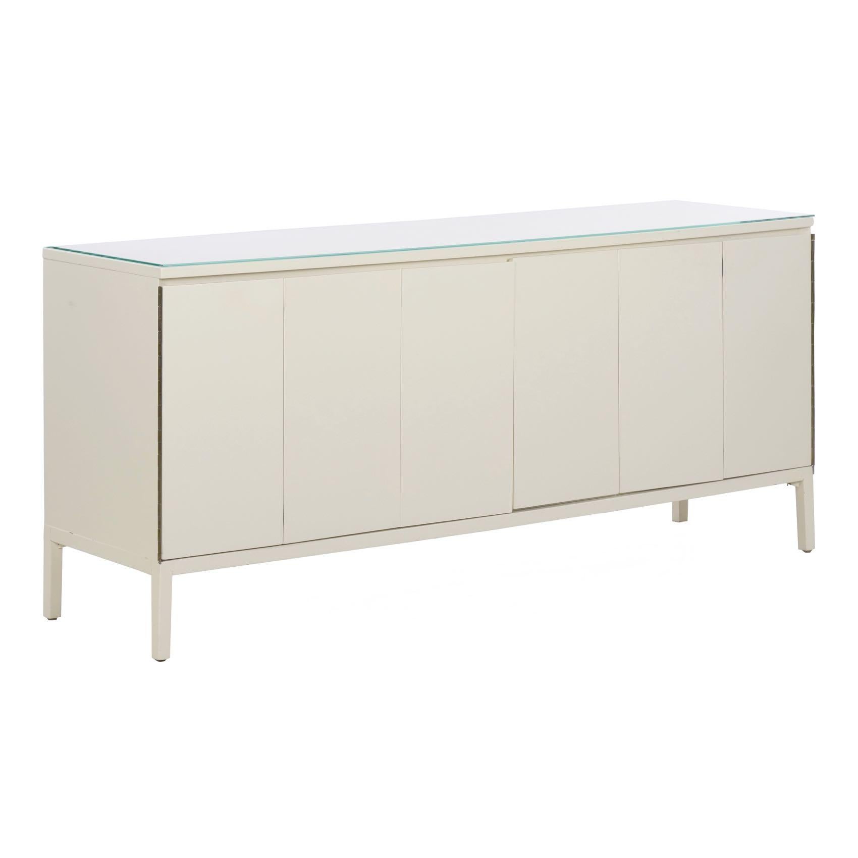 This lovely modernist cabinet is a picture of simplicity and austerity. Finished in a hard white lacquer and topped by a piece of clear glass, the credenza doors swing outward on full length hinges to reveal a series of eight drawers. All are