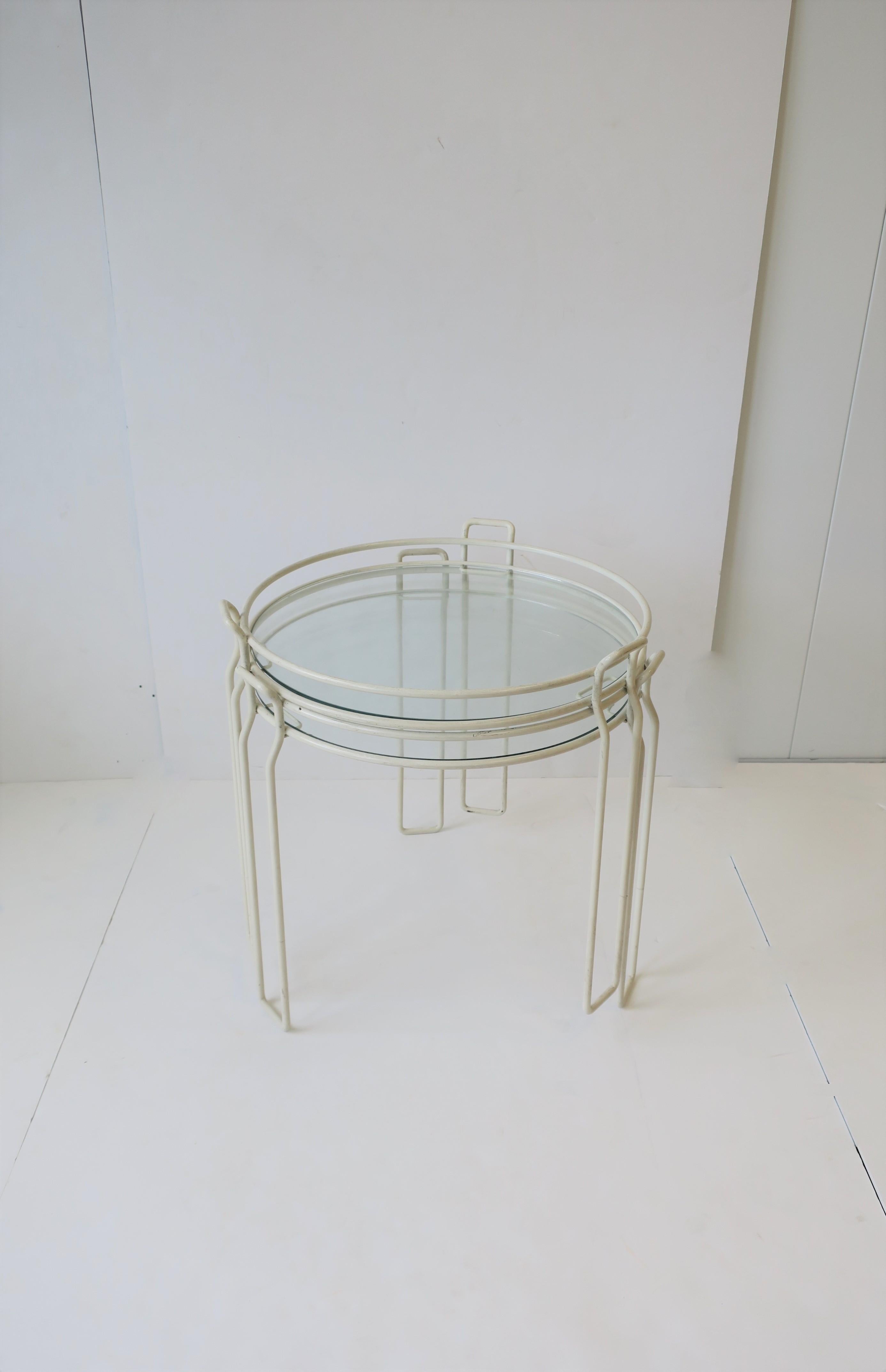 A chic set of two (2) Modern style or Mid-Century Modern period nesting/stacking or side drinks small tubular white tables, circa 1960s. Tables are white enamel metal frames with circular glass tops, and three small handles for easy lifting or