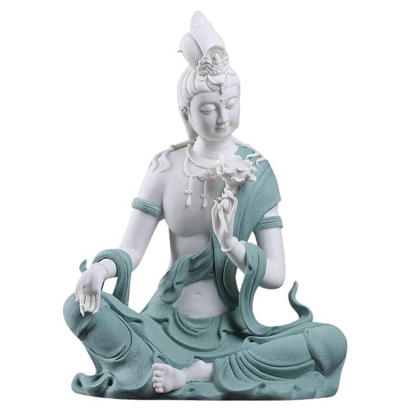 Moderner sitzender Buddha aus weißem Porzellan in blauem Gewand, der eine Lotusblume hält