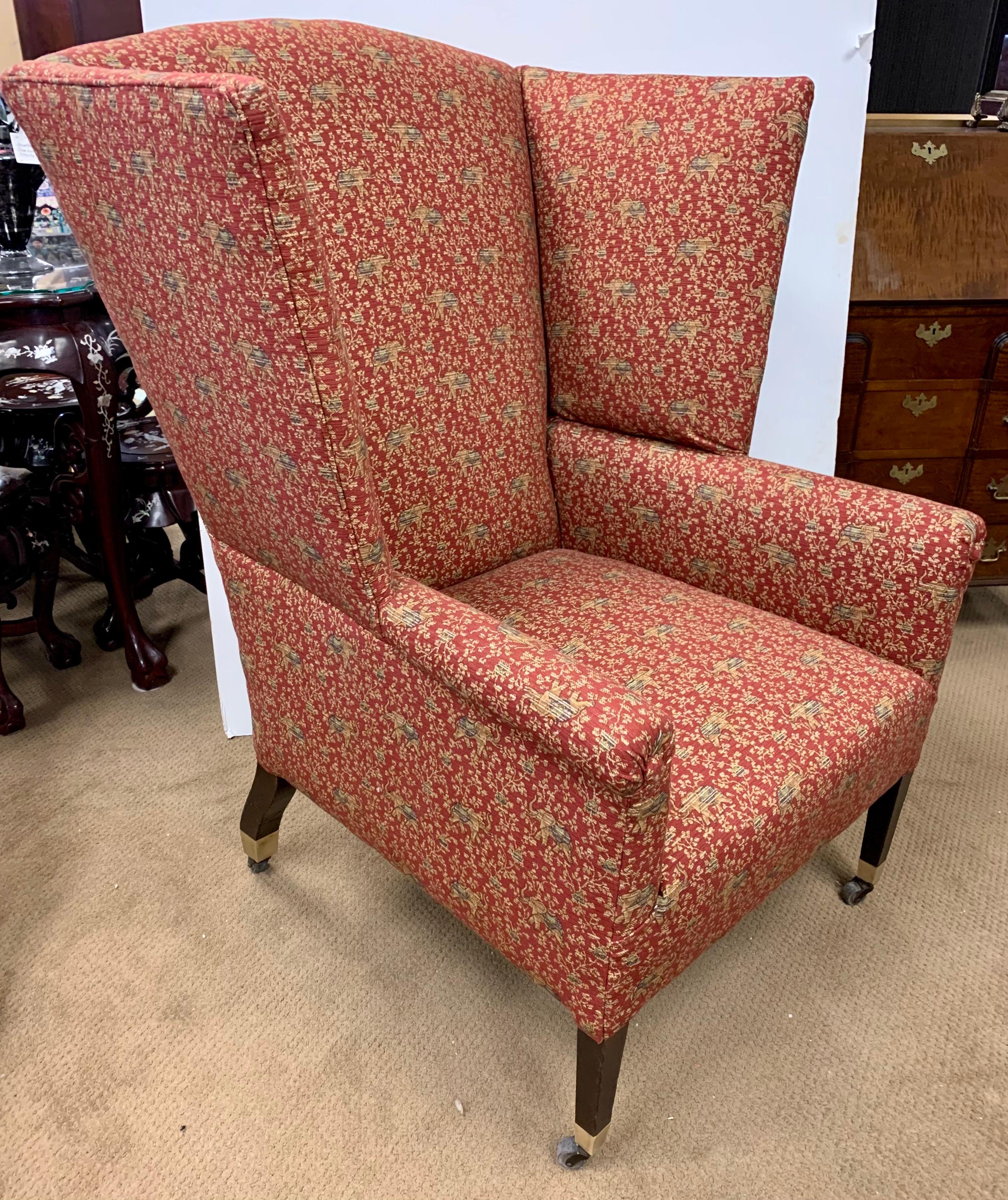 A modern take on the Classic wingback, with a larger profile that invites you to sink in. It is upholstered in a red chinoiserie print fabric with elephants. On brass castors for ease of movement.