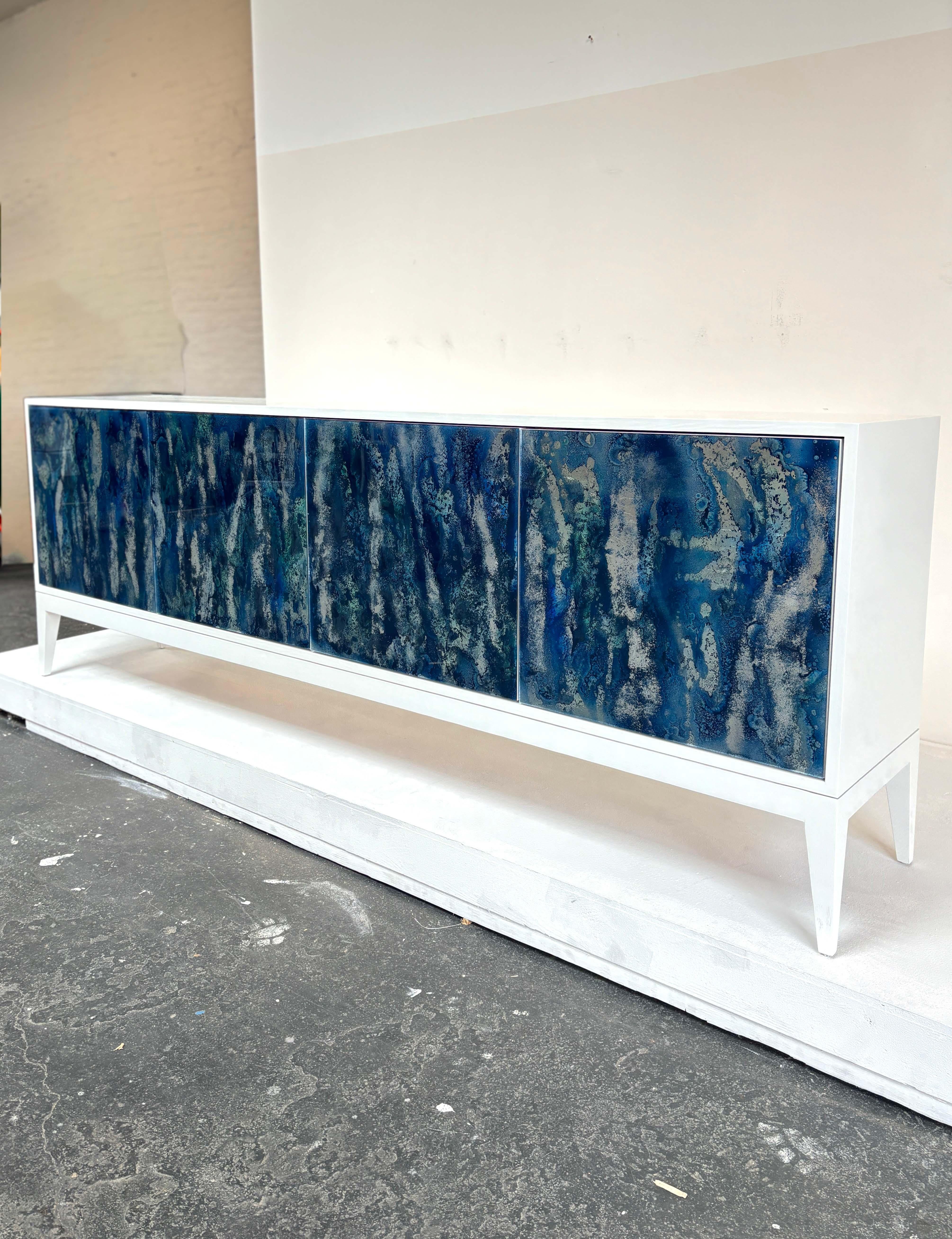 The Milano Mystic Buffet by Ercole Home has 4-doors with touch latch, each with hand-painted Midnight Summer Mystic Glass, and a White Painted finish on Oak. 

Adjustable interior shelving in each compartment. 

Custom sizes and colors available.