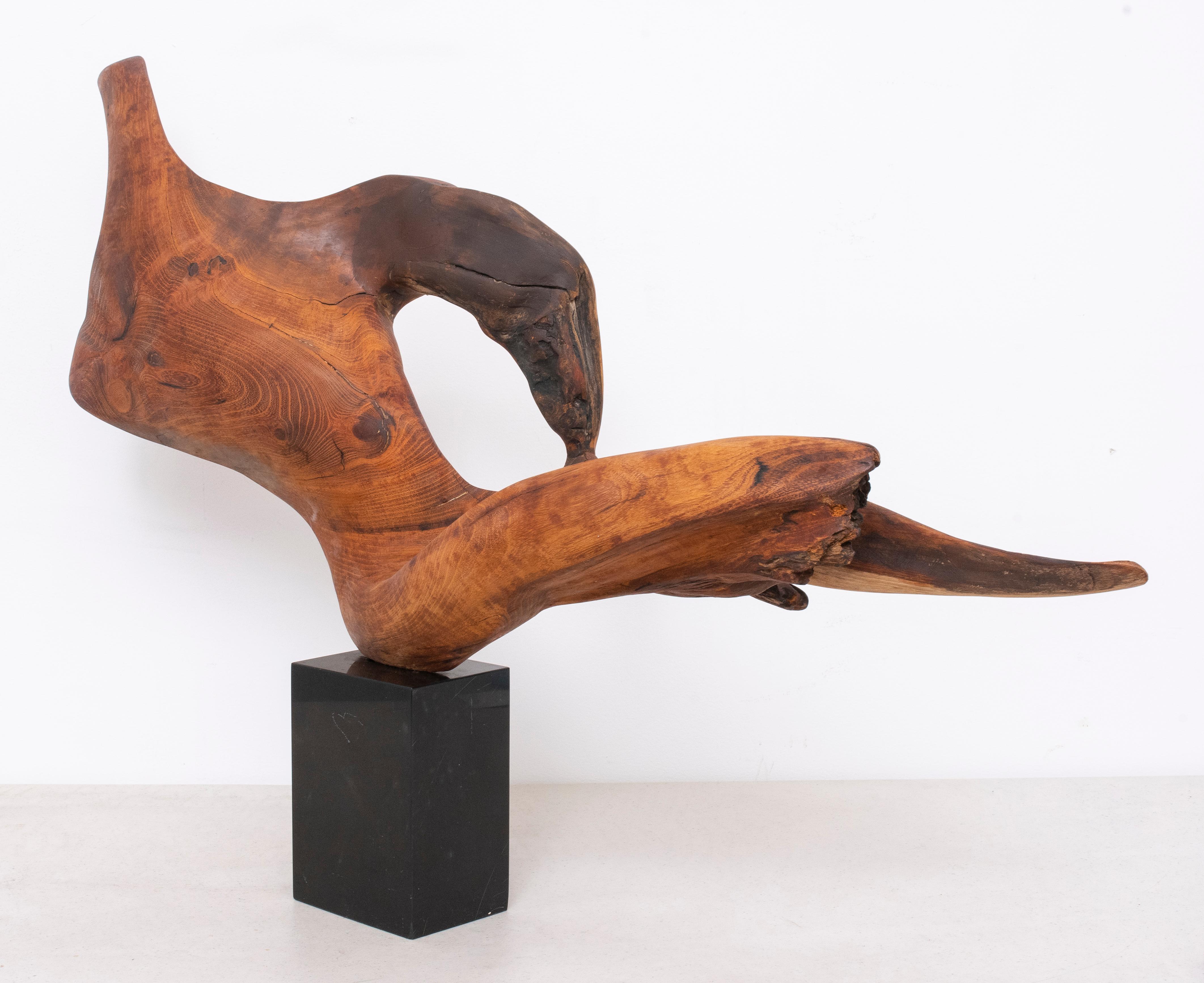 Modern abstract wood sculpture of flowing form resembling a reclining headless figure with burled grain, mounted upon a black marble base, no visible signature. 20.1