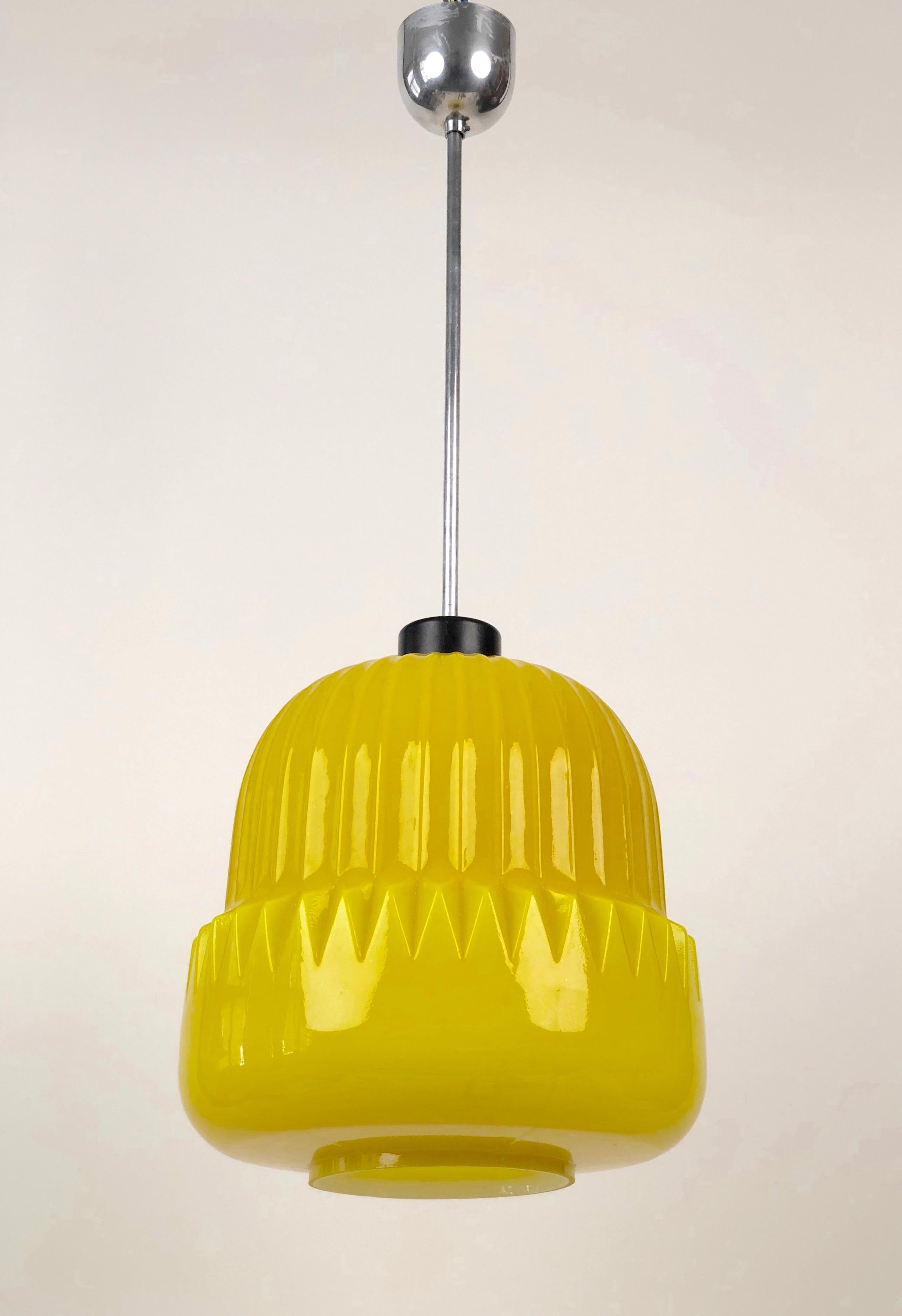 Une lampe suspendue unique du début des années 1960, fabriquée en Tchécoslovaquie. L'abat-jour en verre jaune présente un motif cannelé moulé dans la forme du verre. La lumière émise est chaude et intense. Il brille. J'espère que j'ai réussi à