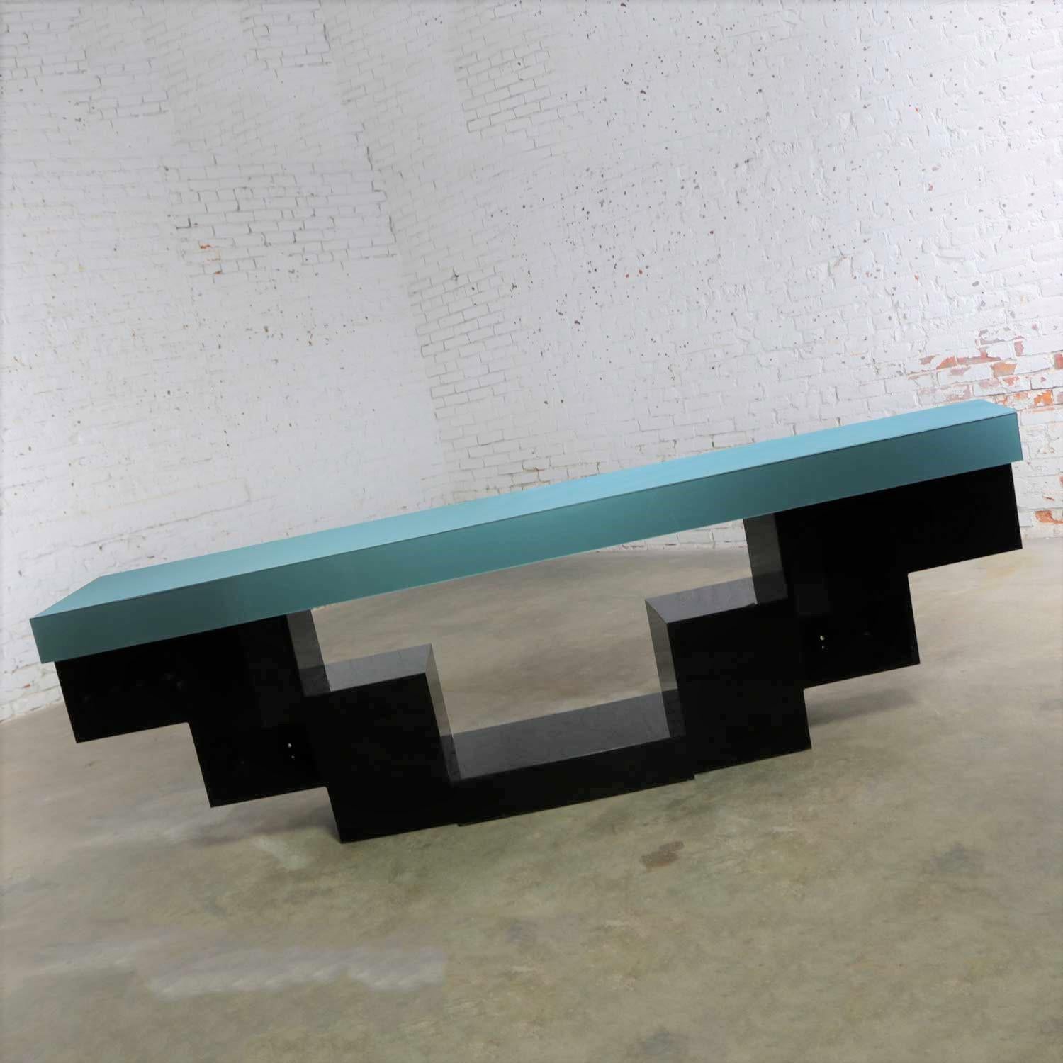 Handsome modern console table or credenza with a zig-zag or stepped profile and clad in black and teal plexiglass. It is in wonderful vintage condition with only normal wear and no outstanding flaws. There is a small flaw in the teal plexi on the