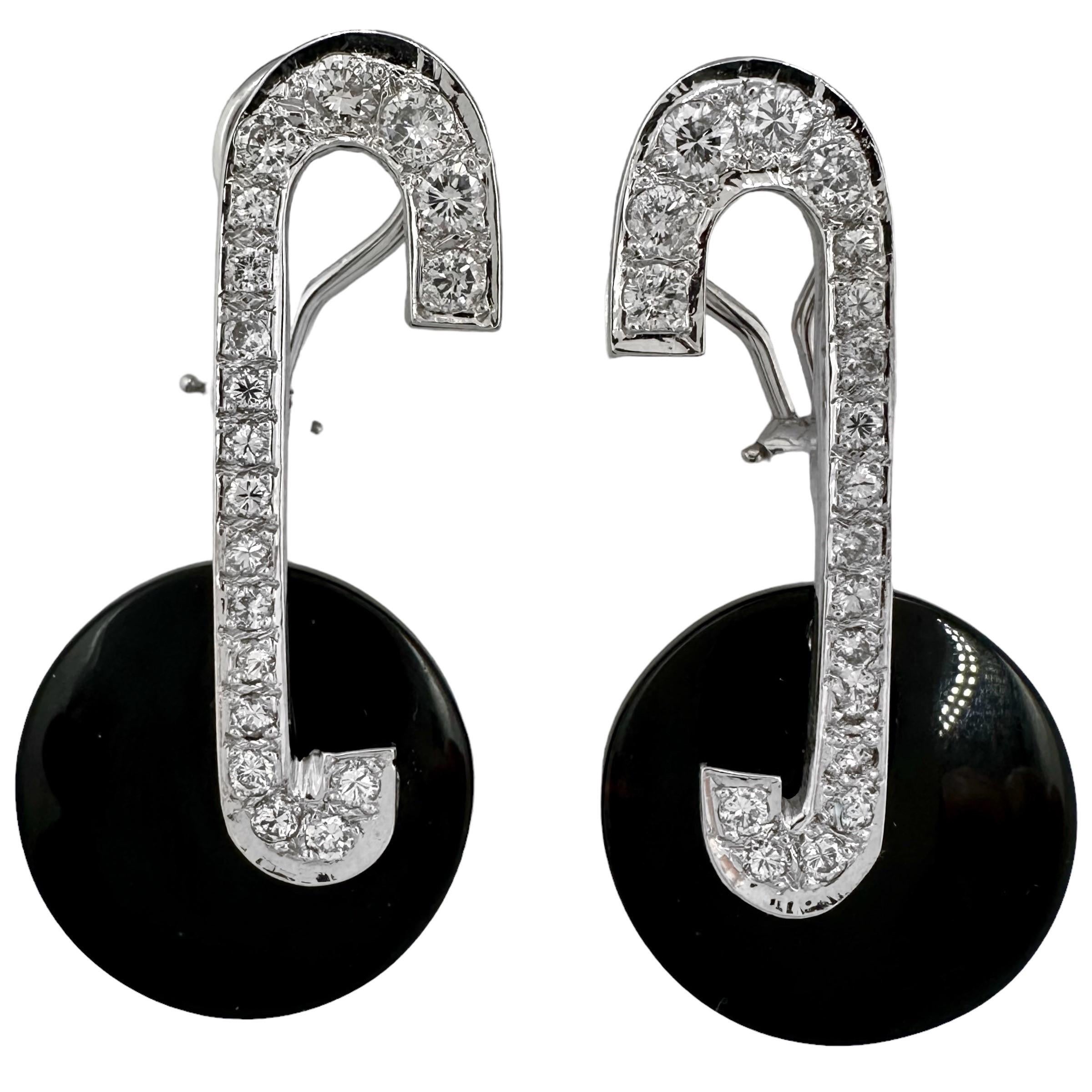 This Modernist pair of 14k white gold fashion earrings are set with a line of brilliant cut diamonds in the form of the letter C, from which 13/16 inch diameter round black onyx discs attach at the bottom. Total approximate diamond weight is 1.25ct