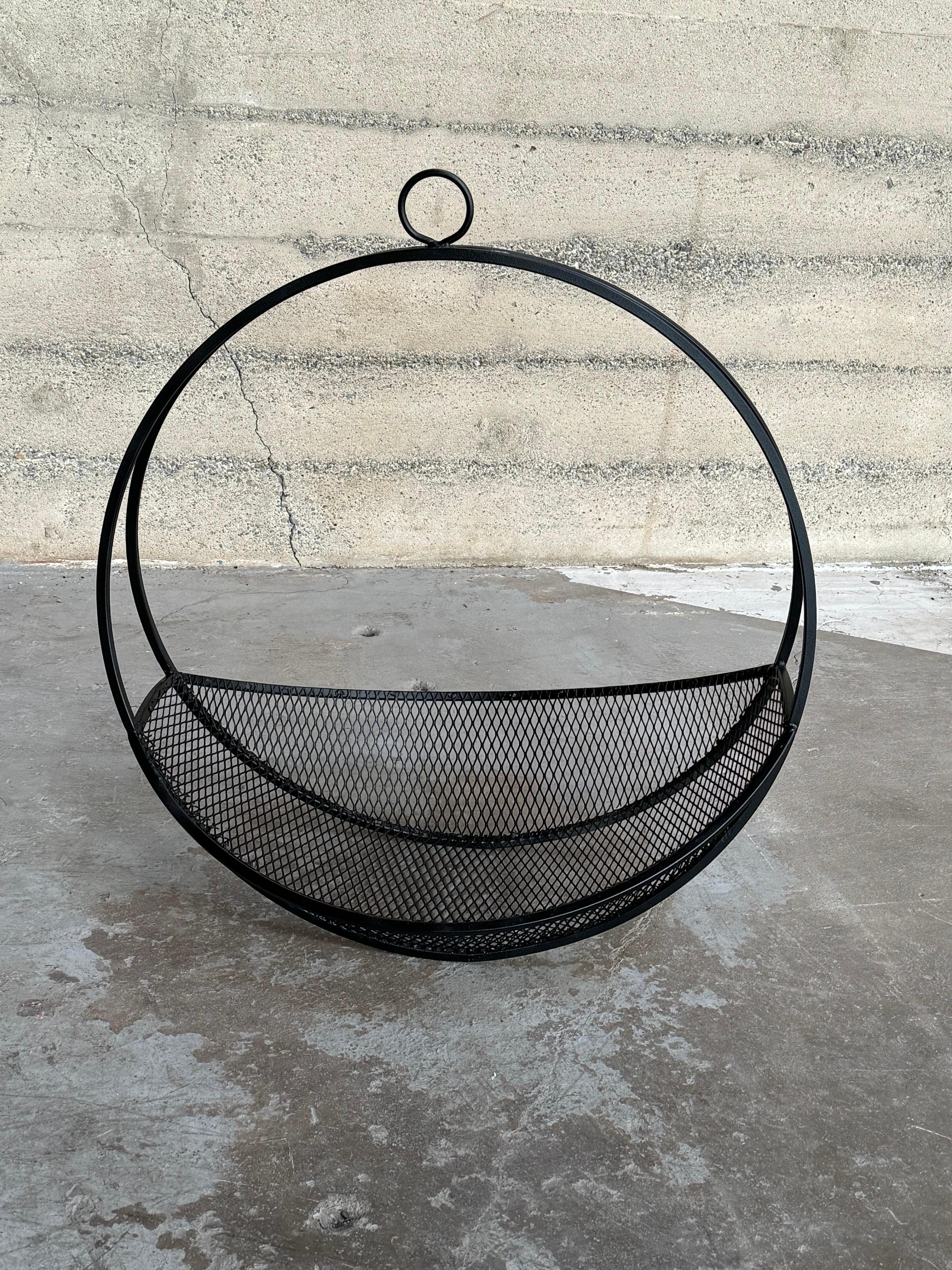 Modernist circa 1950s expanded metal hanging fireplace log holder. The circular shape is created by two squared metal rods with a circular ring welded at the top for hanging and the basket is constructed of an expanded metal mesh tapered at both