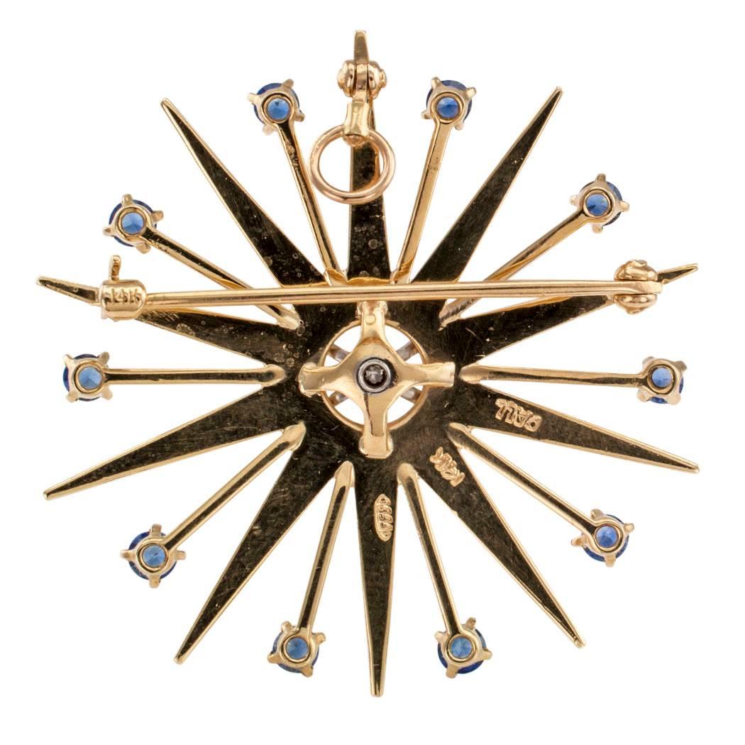 Modernist 1950s sapphire diamond gold and palladium brooch pendant.  The mid-century design features ten sapphires totaling approximately 1.00 carat, radiating from a central axis set with a single diamond weighing approximately 0.13 carat,