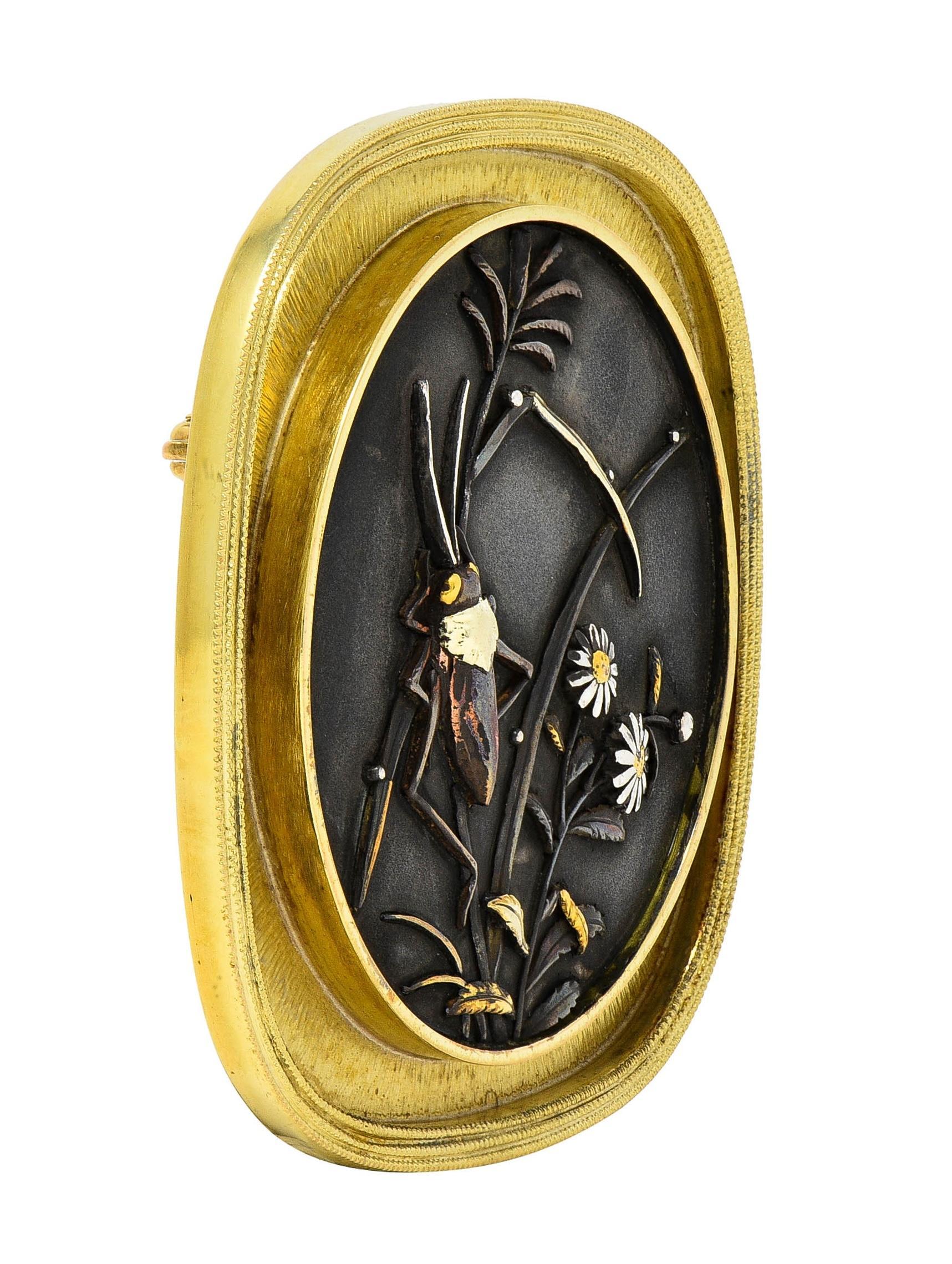 Centering a 36.5 mm round Japanese Shakudo tablet depicting a grasshopper and daisies 
Comprised of silver, yellow gold, copper, and green gold with varying patinas
Bezel set with a recessed cushion-shaped surround 
Accented by fine radial and